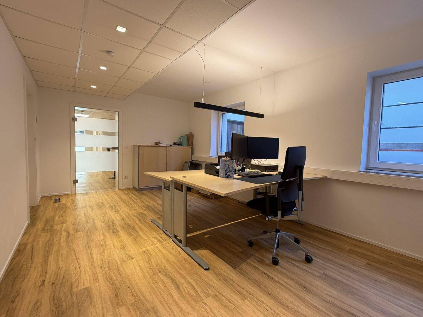 Geräumiges Büro mit mehreren Arbeitsplätzen, abgehängter Decke und Laminatboden.