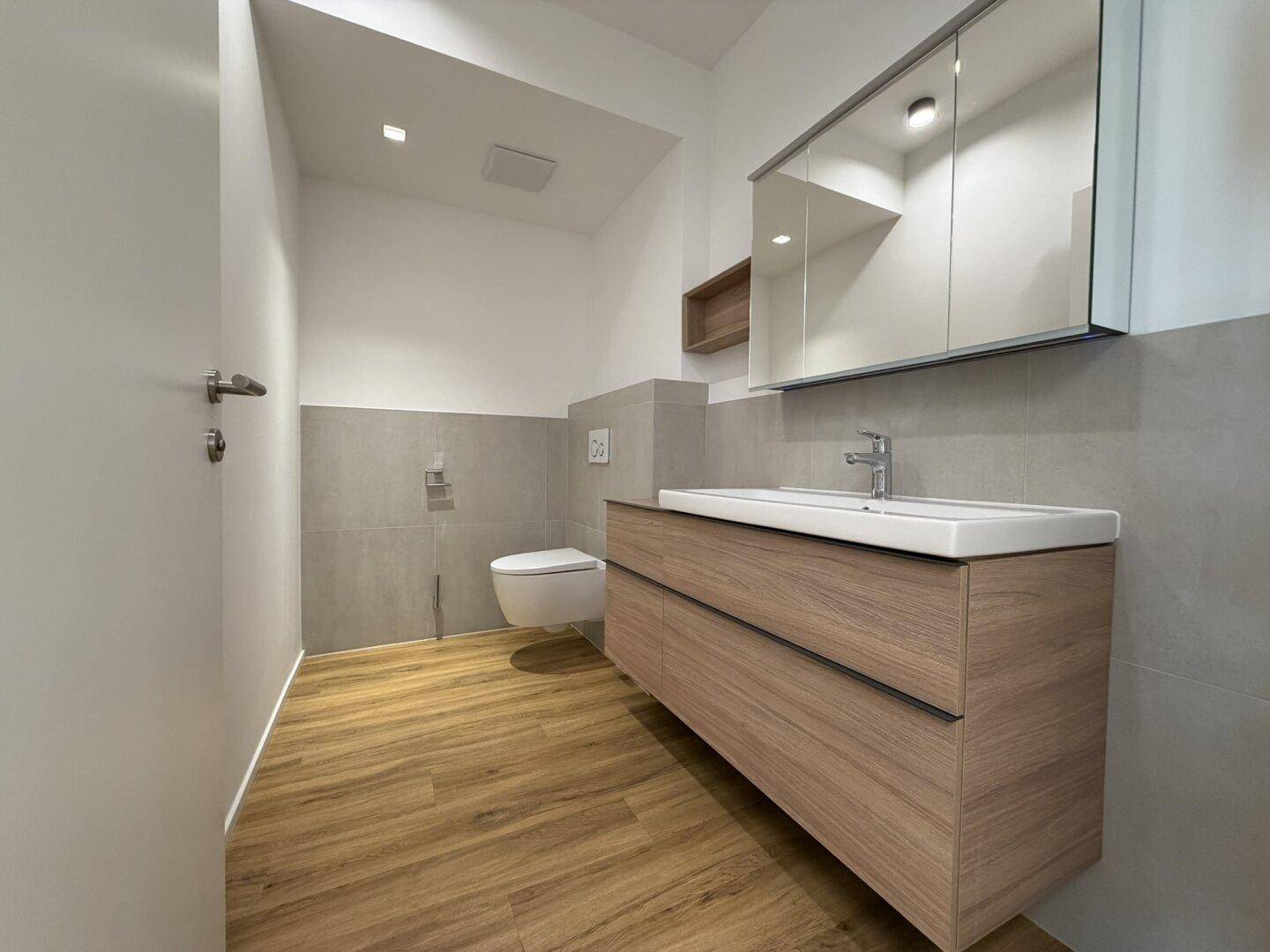 Modernes Badezimmer mit schwebendem Waschtisch, Spiegelschrank und hellen Fliesen.