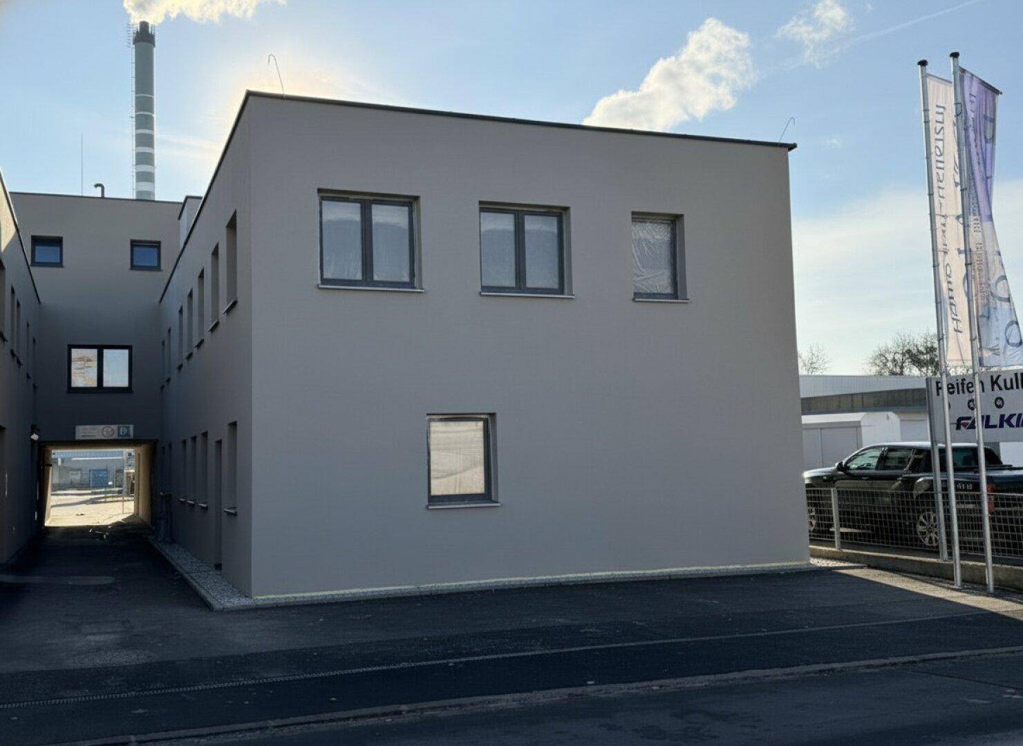 Seitenansicht eines modernen Neubaus mit grauer Fassade und großen Fenstern.