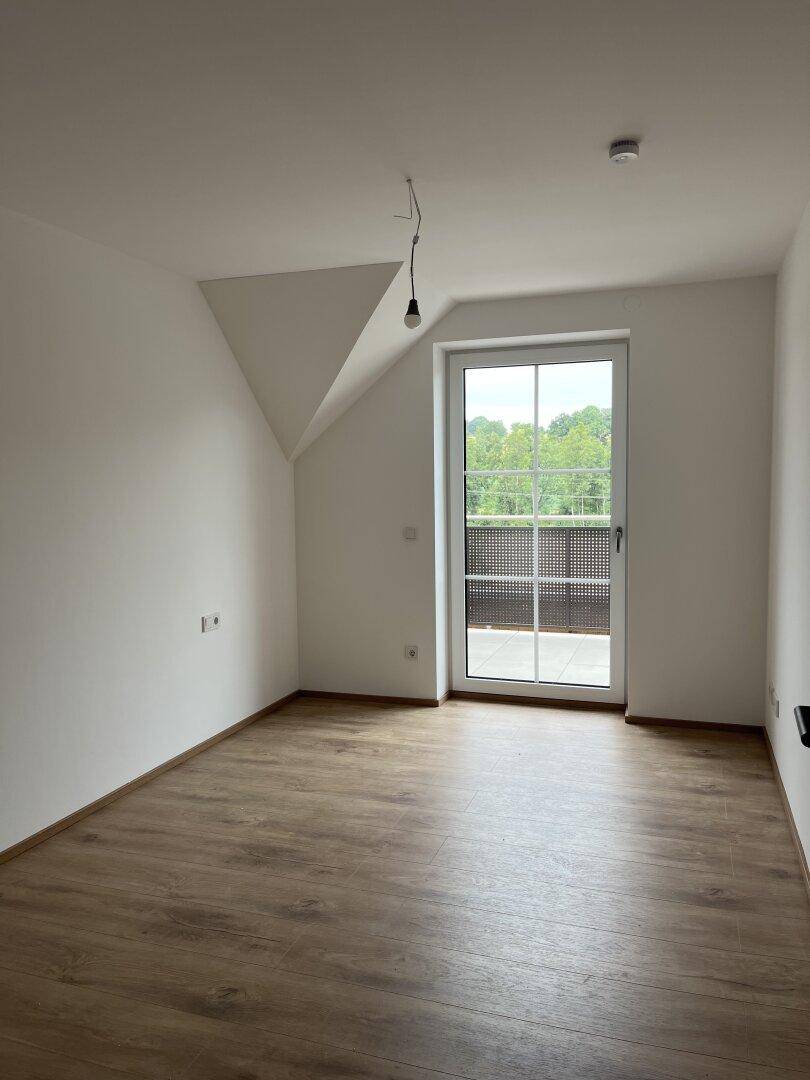 Helles Zimmer mit Laminatboden, Dachschräge und Zugang zu einem Außenbereich.