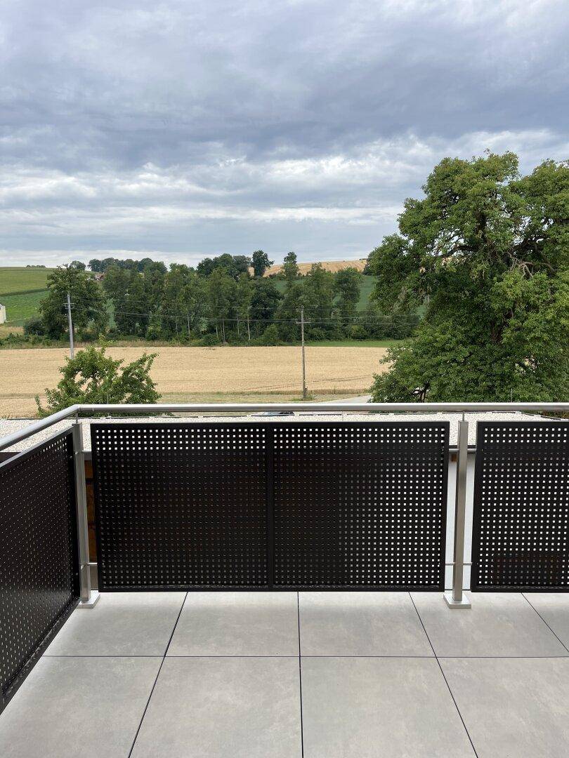 Heller Balkon mit Metallgeländer und unverbautem Blick auf die umliegende Natur und Felder.