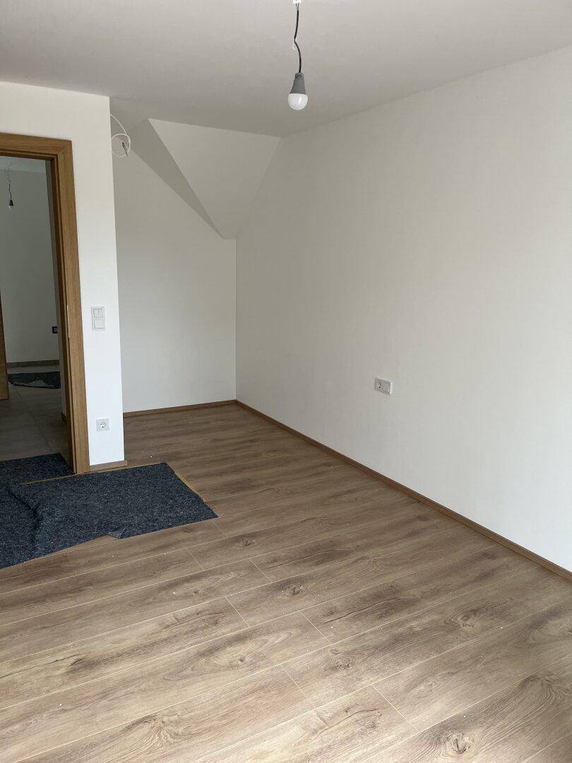 Geräumiges Zimmer mit hellem Laminatboden, weißen Wänden und Dachschräge, bereit zum Einrichten.