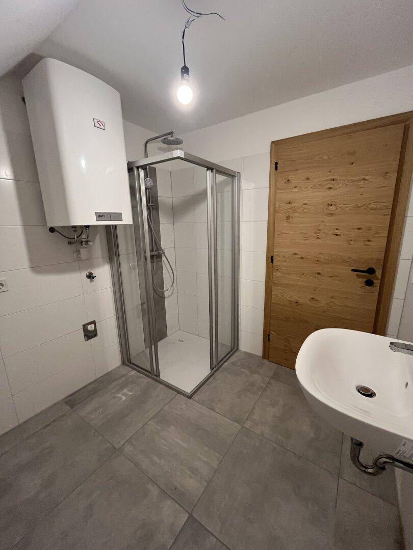 Modernes Badezimmer mit Duschkabine, Waschbecken und Wandfliesen in neutralen Farbtönen.