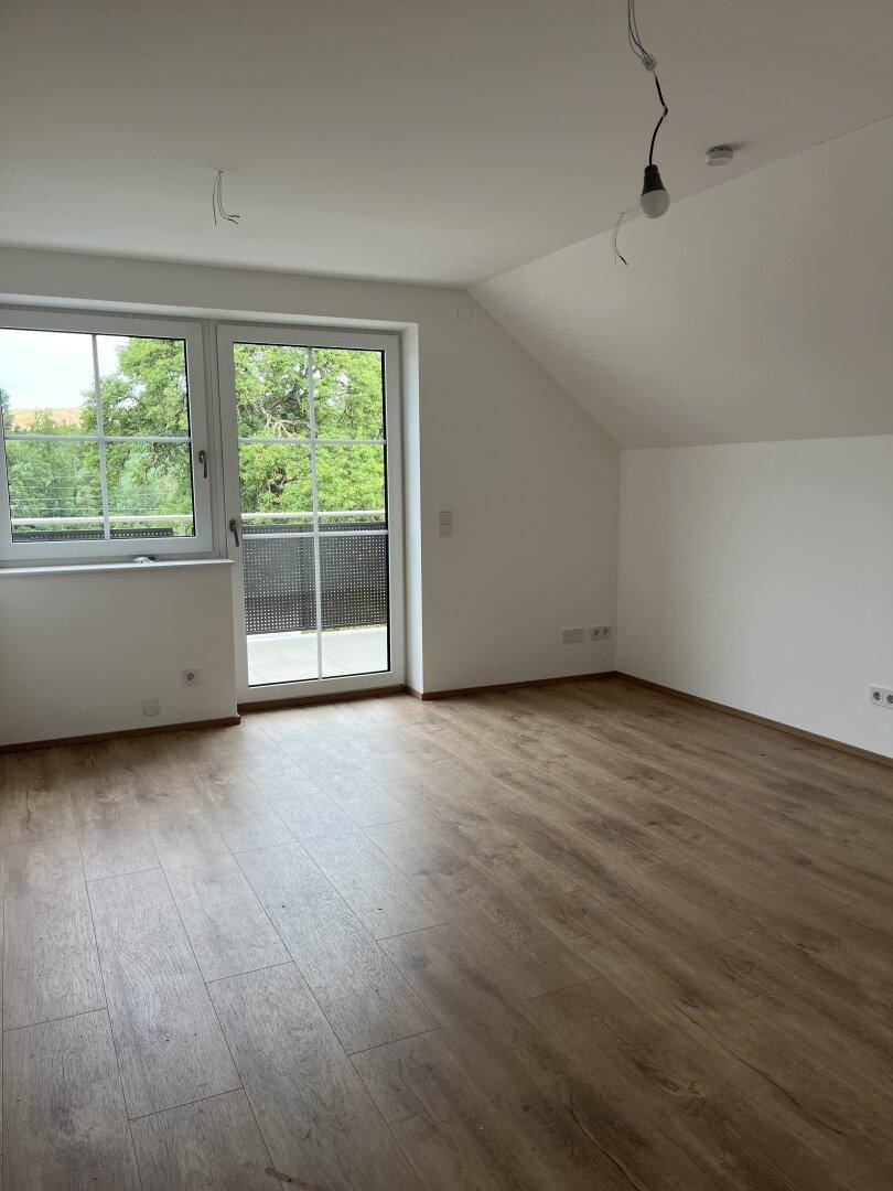 Lichtdurchflutetes Zimmer mit modernem Laminatboden und direktem Zugang zum Balkon.