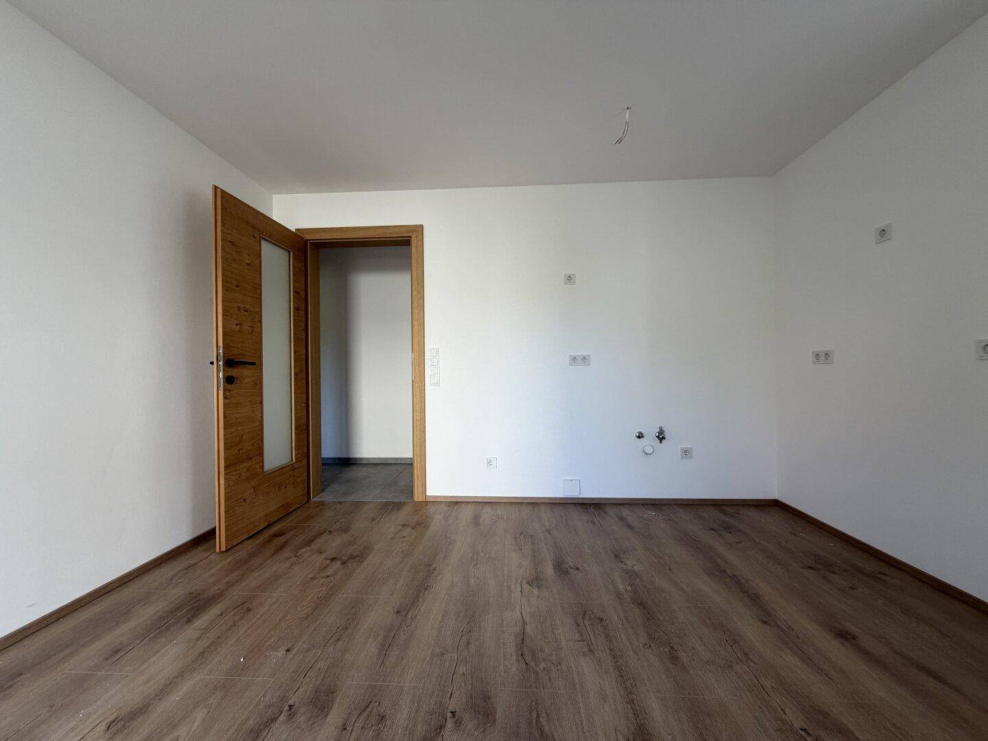 Leerer Raum mit Laminatboden und weiß gestrichenen Wänden, bereit für die Einrichtung.