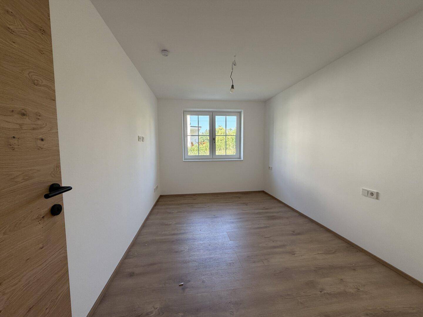 Schlafzimmer mit Laminatboden, weißen Wänden und einem Fenster für Tageslicht.