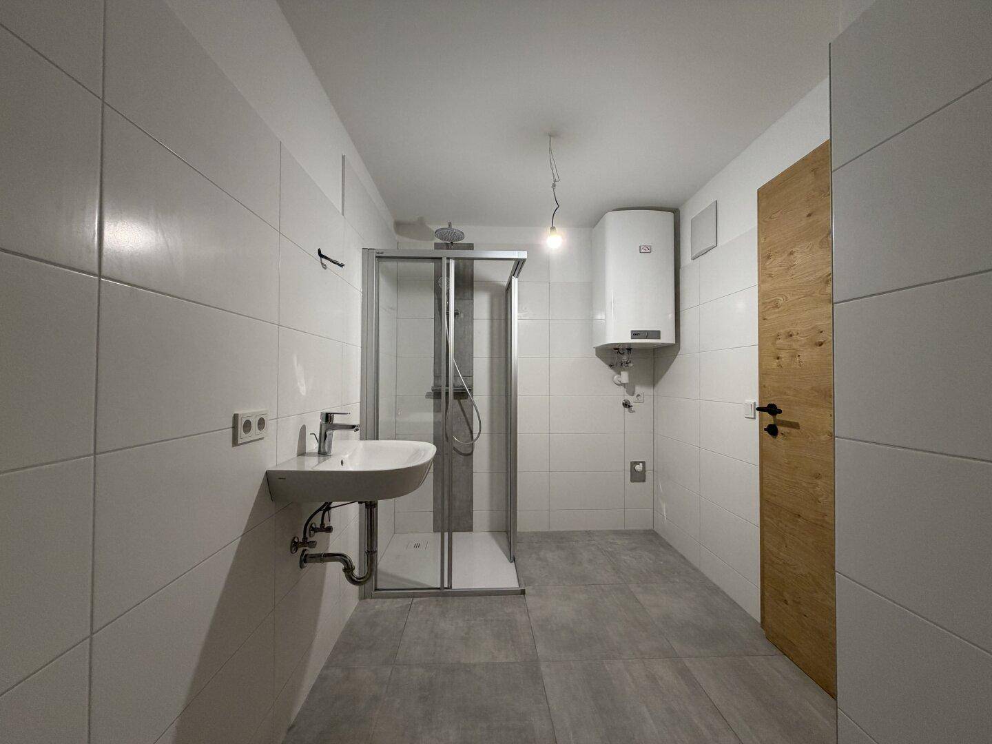 Modernes Badezimmer mit weißen Fliesen, Duschkabine und wandhängendem Waschbecken.
