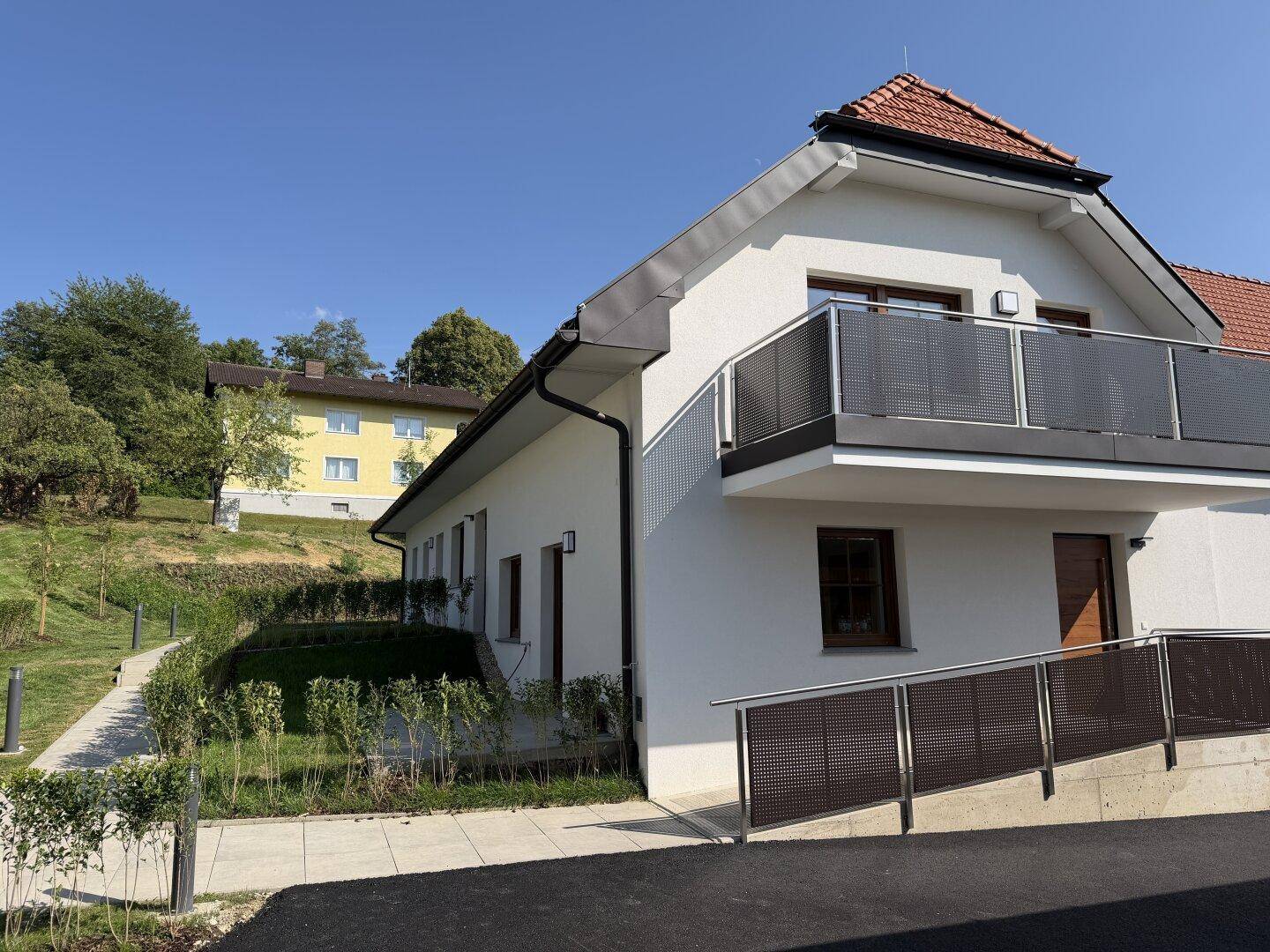 Seitenansicht des Neubaus mit Balkon, Rampe und gepflegter Außenanlage.