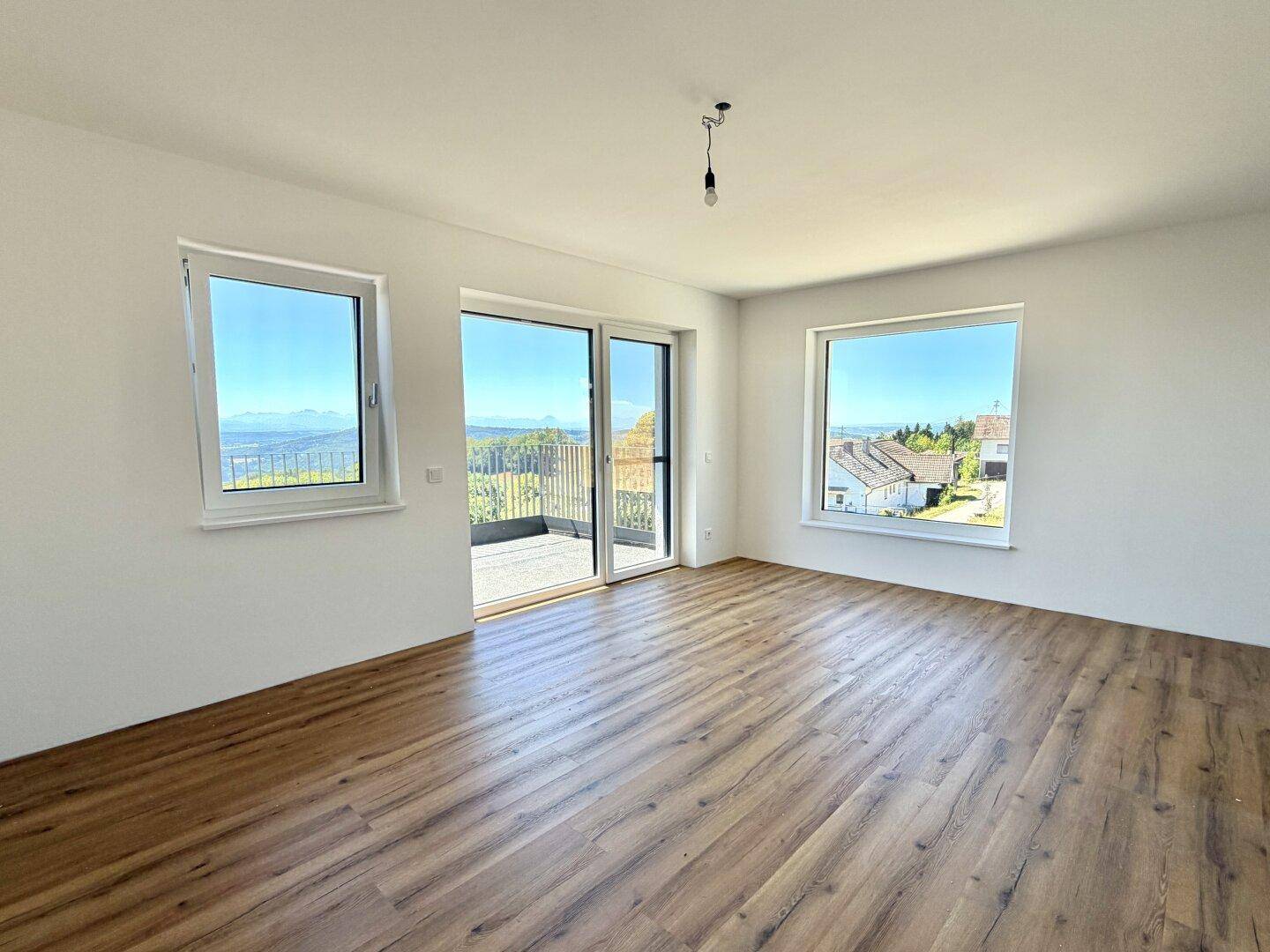 Lichtdurchfluteter Raum mit Panoramablick und modernem Laminatboden, ideal für ein Wohnzimmer.