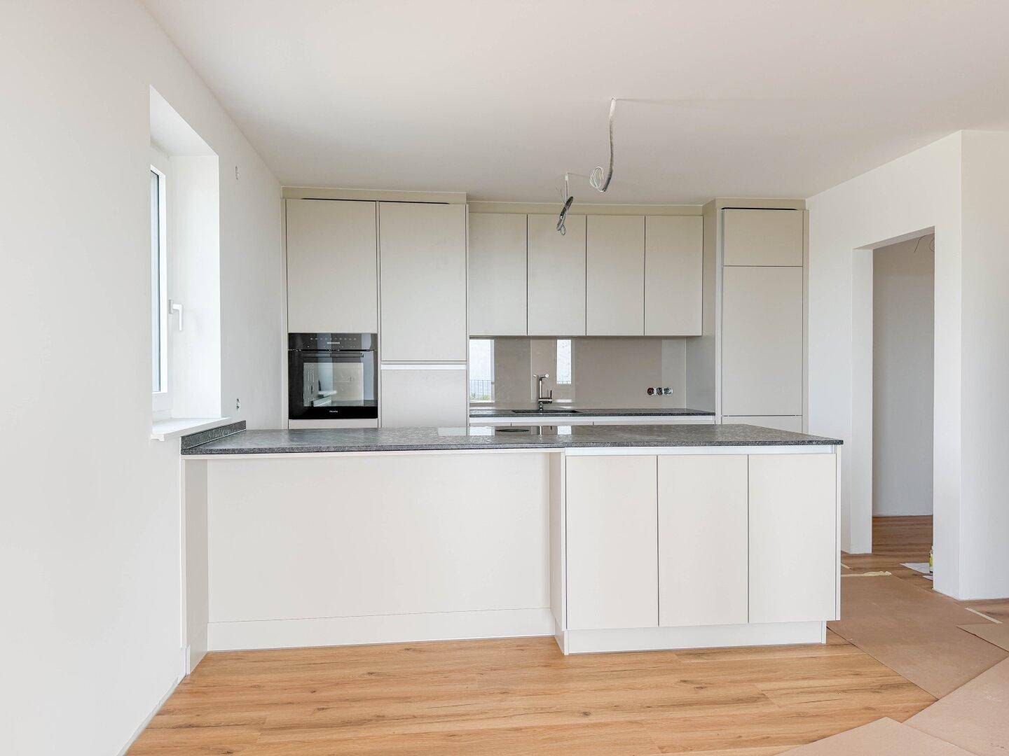 Moderne Einbauküche in hellem Design mit integriertem Backofen und Arbeitsplatte.