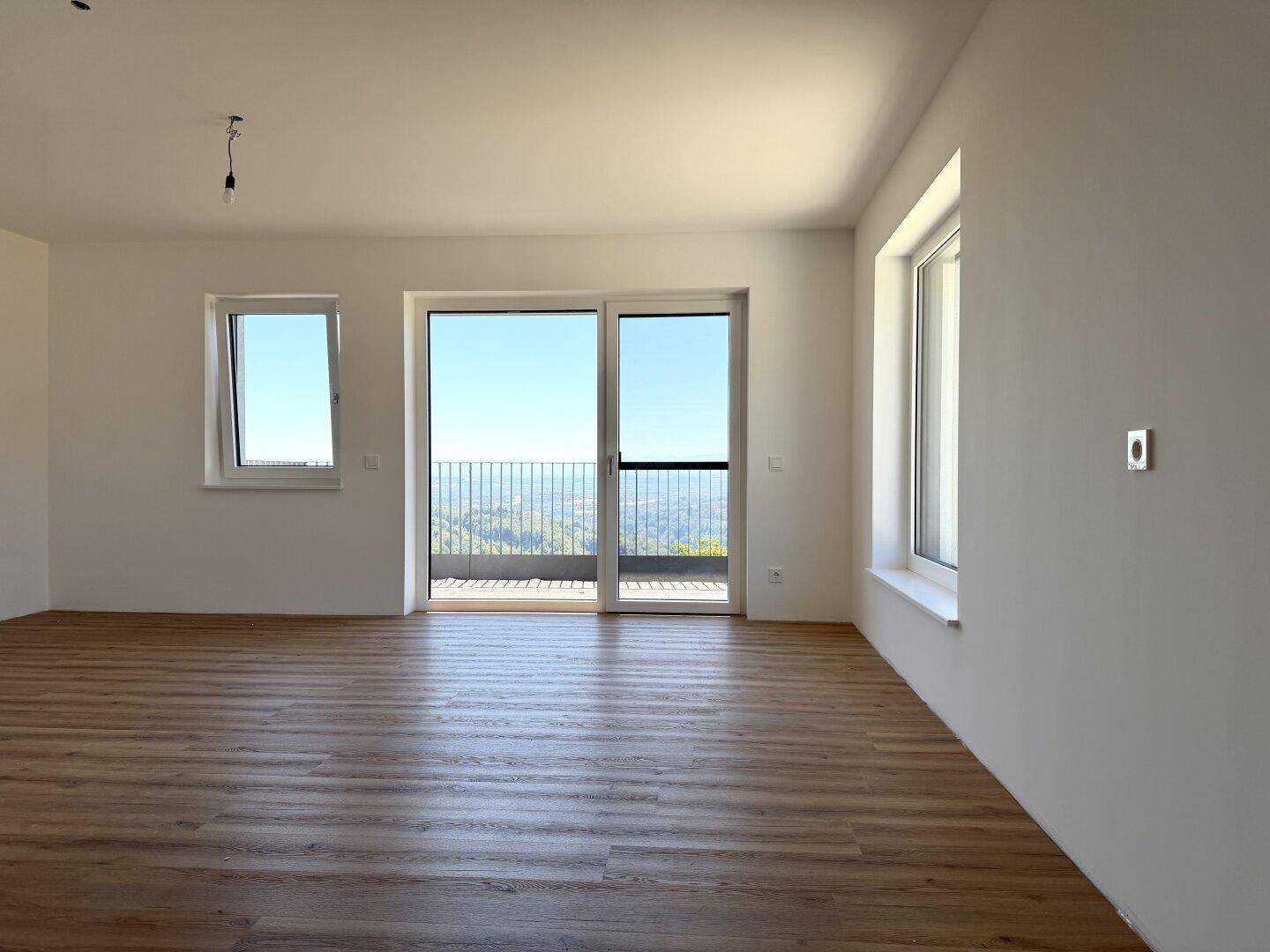 Heller Wohnbereich mit Holzboden, großen Fenstern und Schiebetür zum Balkon mit Panoramablick.
