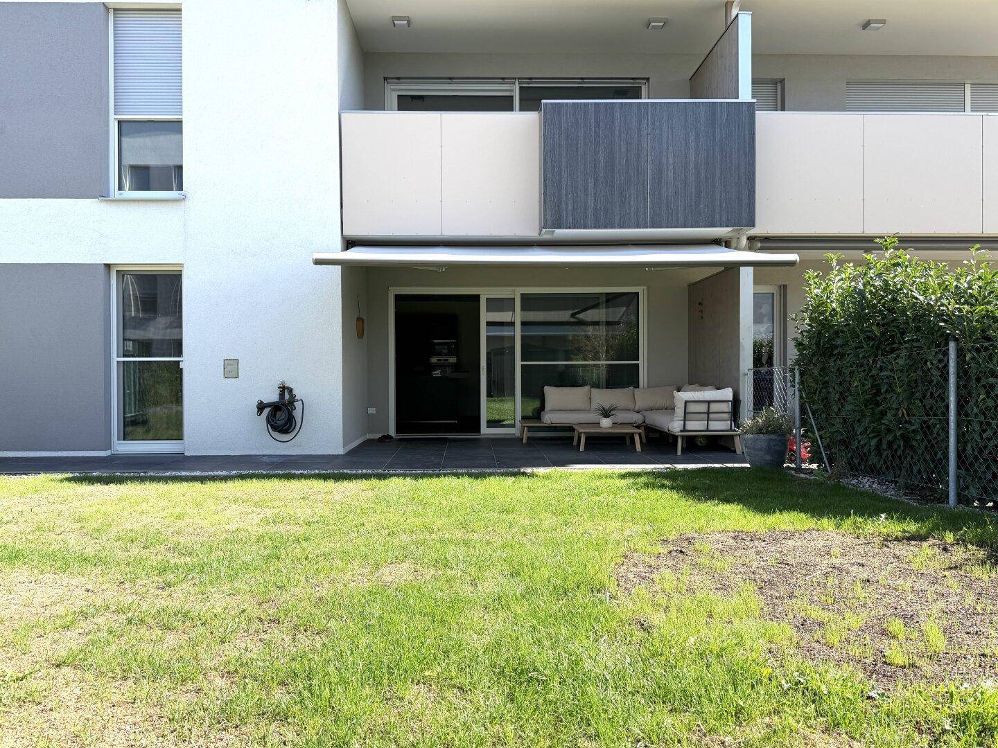 Gebäudefassade mit Terrasse und angrenzendem Gartenbereich, bietet direkten Zugang ins Grüne.