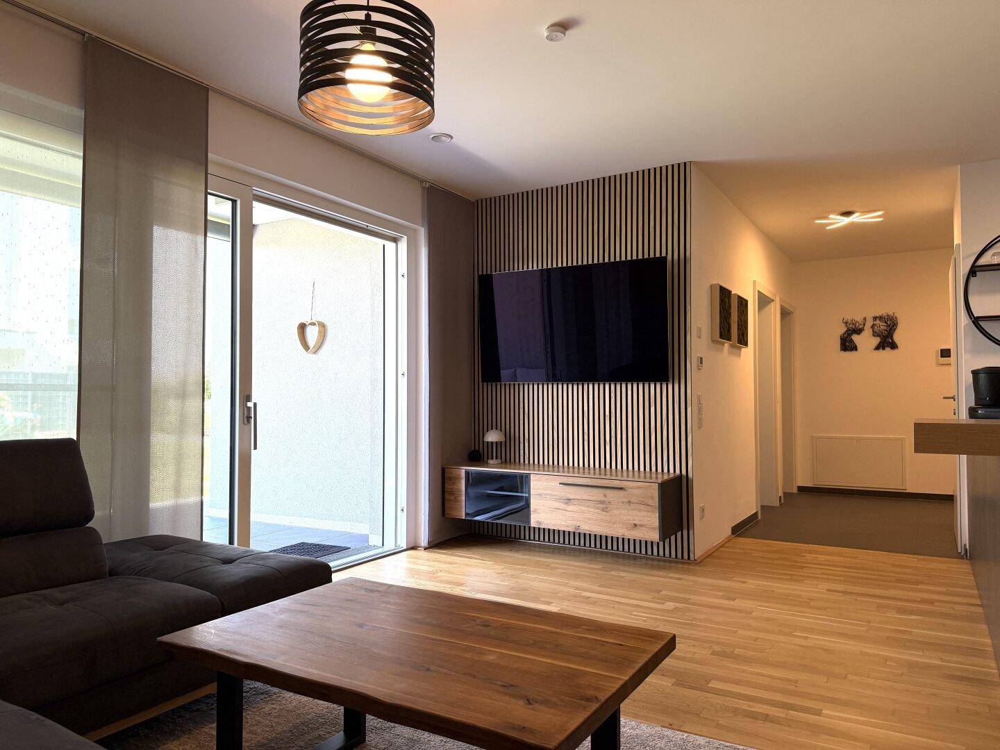 Modernes Wohnzimmer mit Holzboden, stilvoller TV-Wand und Zugang zu einem Außenbereich.