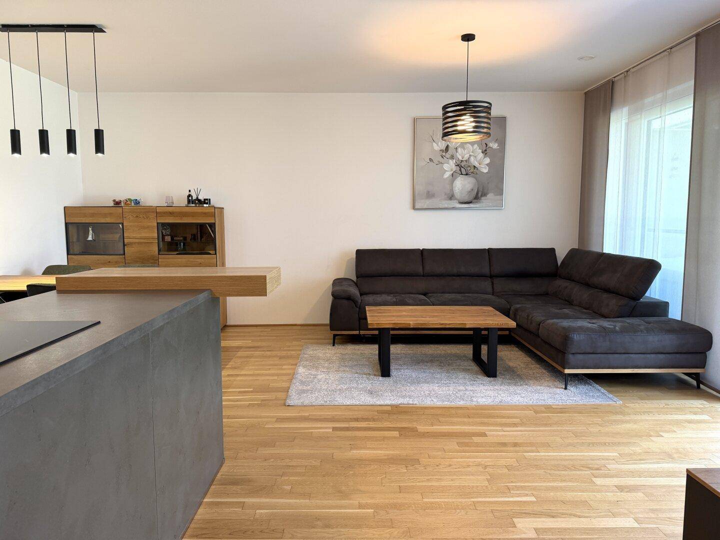 Geräumiger offener Wohnbereich mit Holzboden, großem Sofa und Blick auf die moderne Küche.
