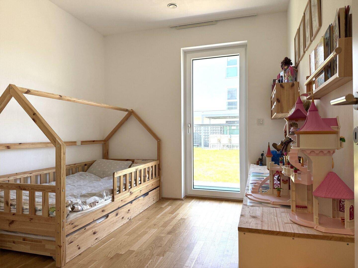 Kinderzimmer mit Holzboden, Hausbett und Zugang zum Garten, hell und freundlich.