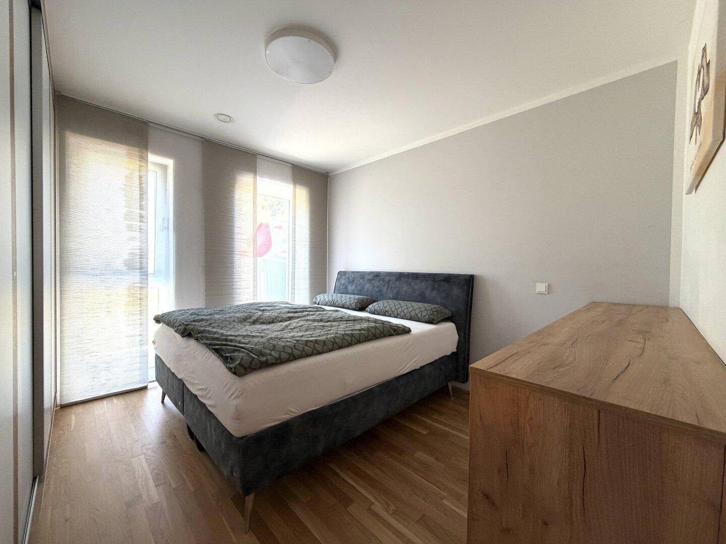 Modernes Schlafzimmer mit Holzboden, Doppelbett und einem Holzschrank, gut beleuchtet.