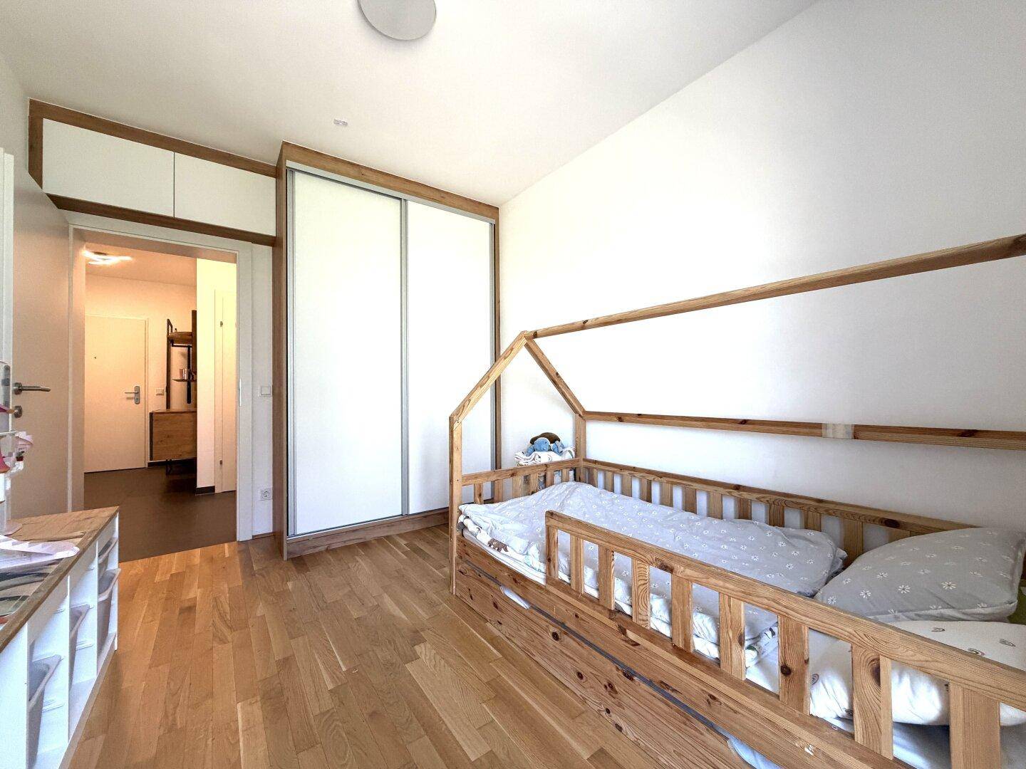 Kinderzimmer mit Holzboden, Hausbett und Einbauschränken, bietet viel Stauraum.