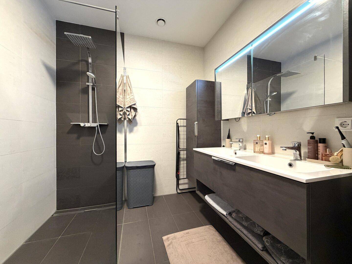 Elegantes Badezimmer mit begehbarer Dusche, modernem Waschtisch und großem beleuchteten Spiegelschrank.