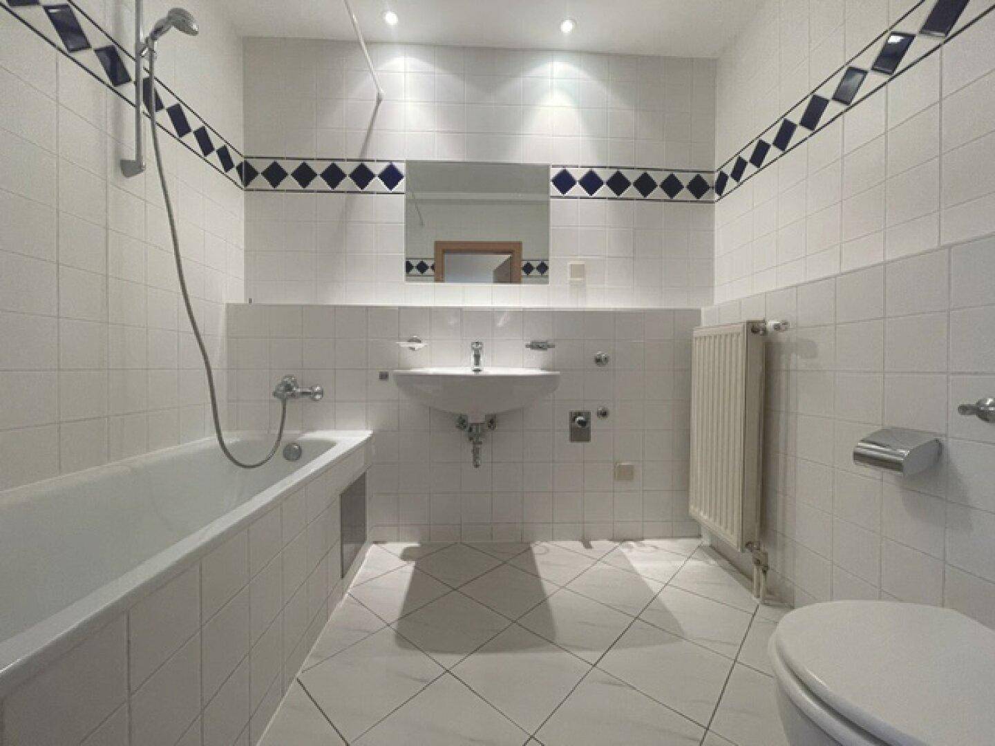 Gefliestes Badezimmer mit Badewanne, Dusche, Waschbecken und WC, akzentuiert durch blaue Bordüren.