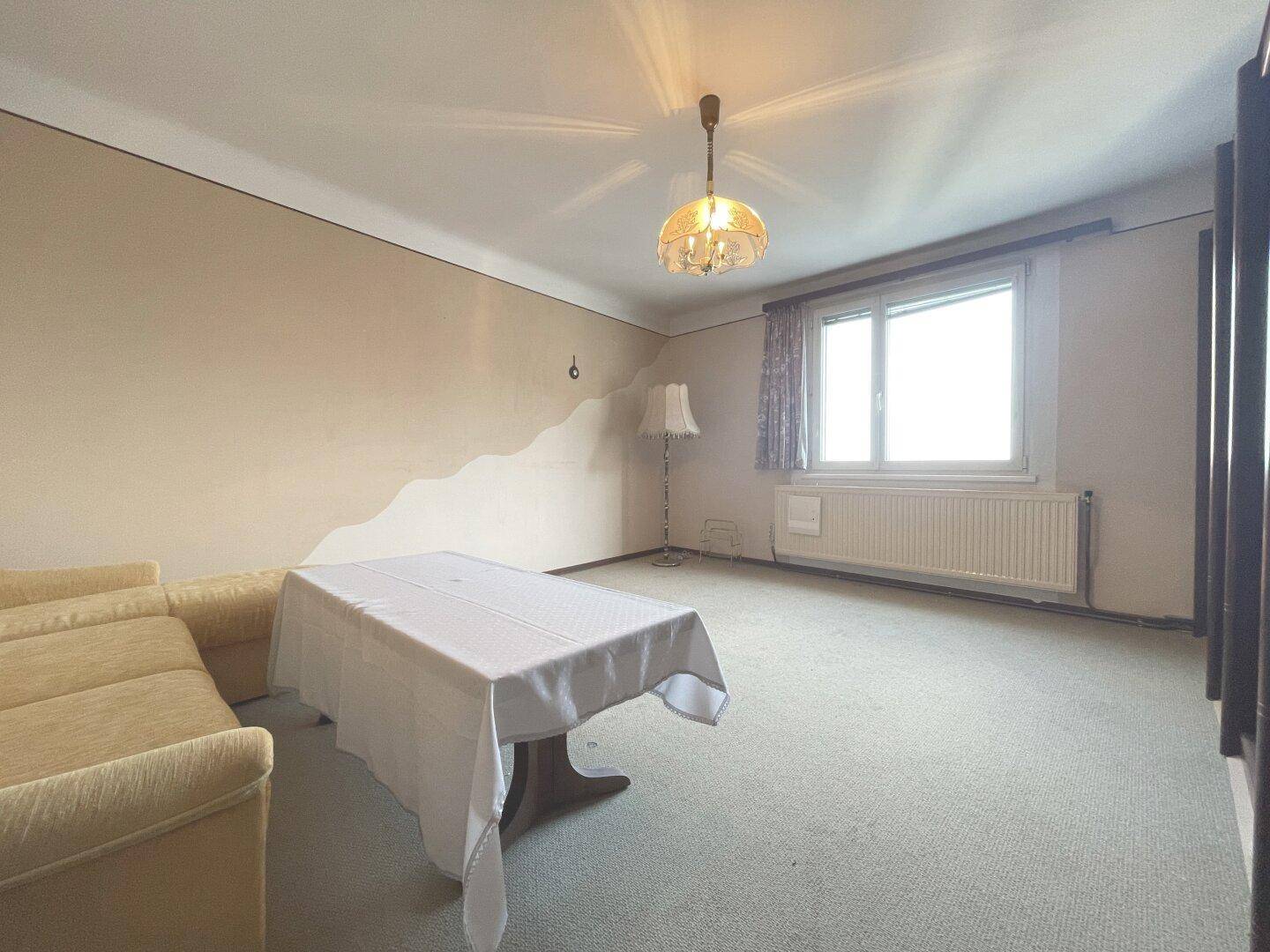 Helles Wohnzimmer mit Teppichboden, Heizkörper und einem Fenster mit Blick nach draußen.