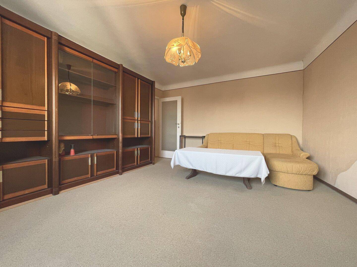 Geräumiges Wohnzimmer mit Teppichboden, Sofa und einer großen Holzschrankwand.