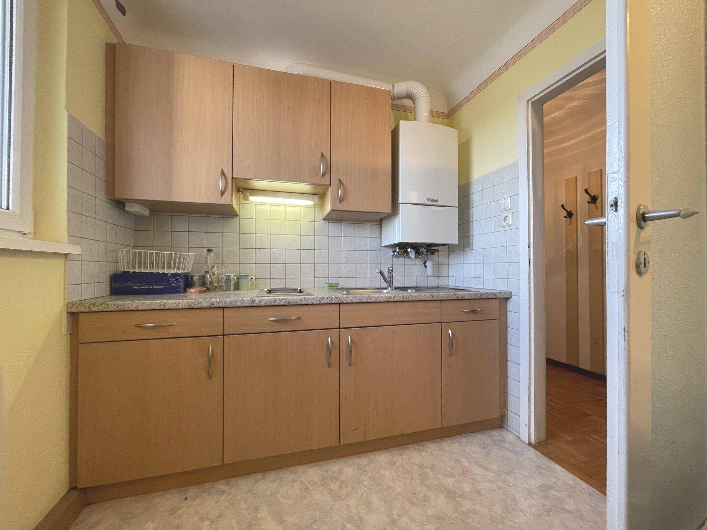 Kleine Küche mit Holzschränken, Spüle und Gastherme an der Wand.