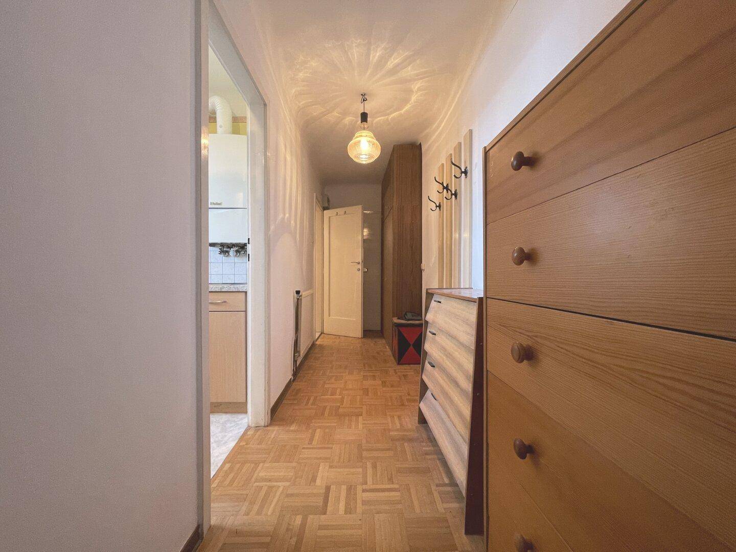 Langer Flur mit Parkettboden, Holzkommode und Garderobe.
