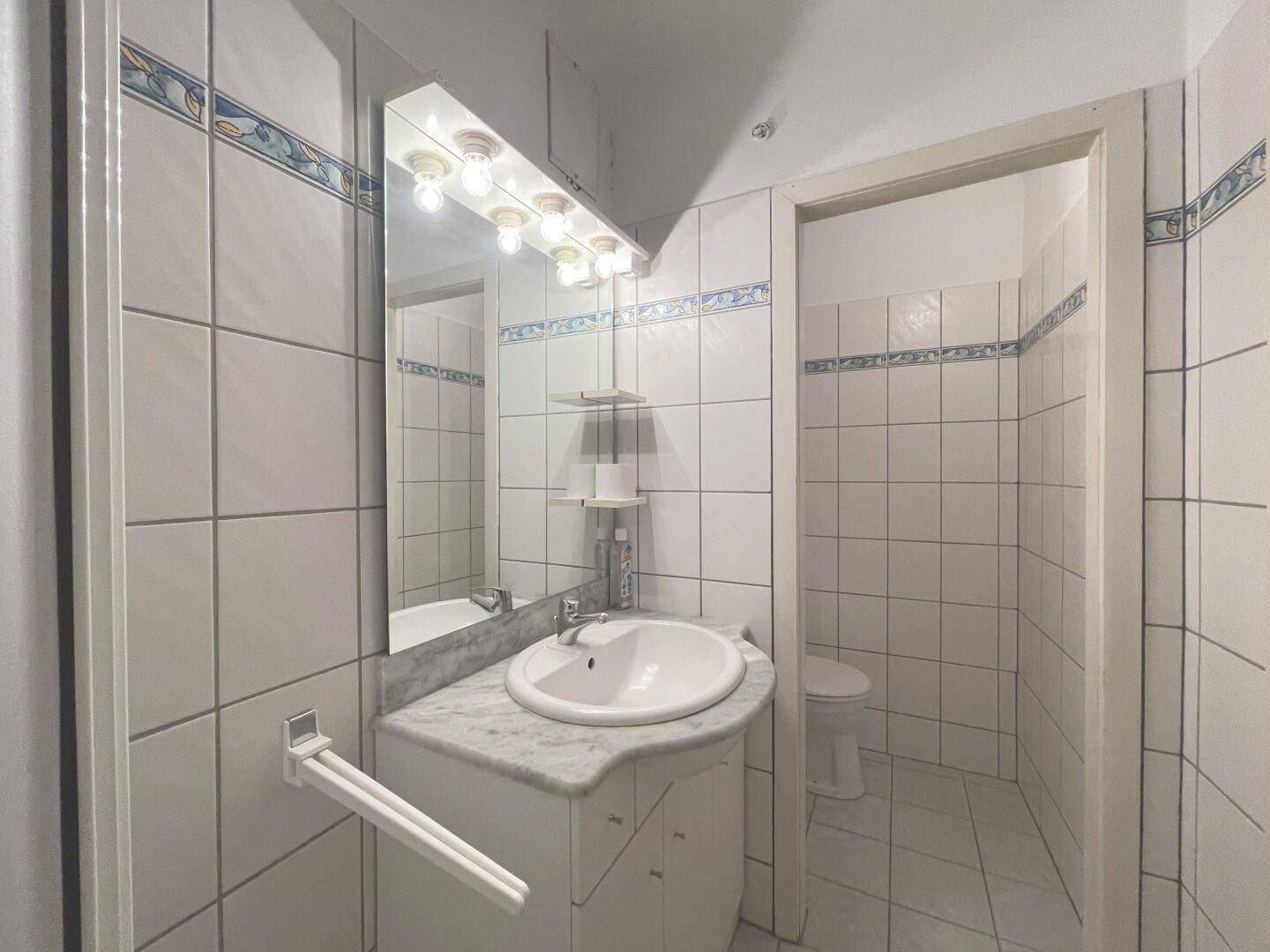 Badezimmer mit weiß gefliesten Wänden, Marmorwaschtisch und Spiegel mit Beleuchtung.