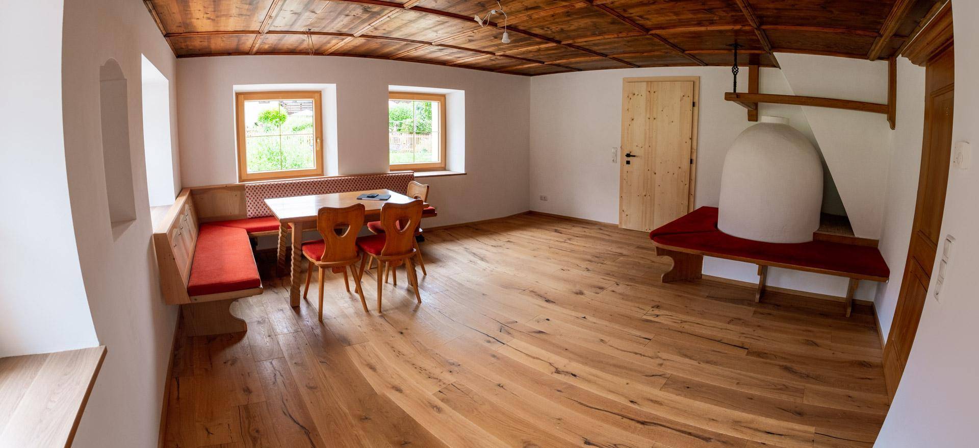 Heller Wohn-Essbereich mit rustikalem Holzboden, Holzkassettendecke und traditionellem Kachelofen.