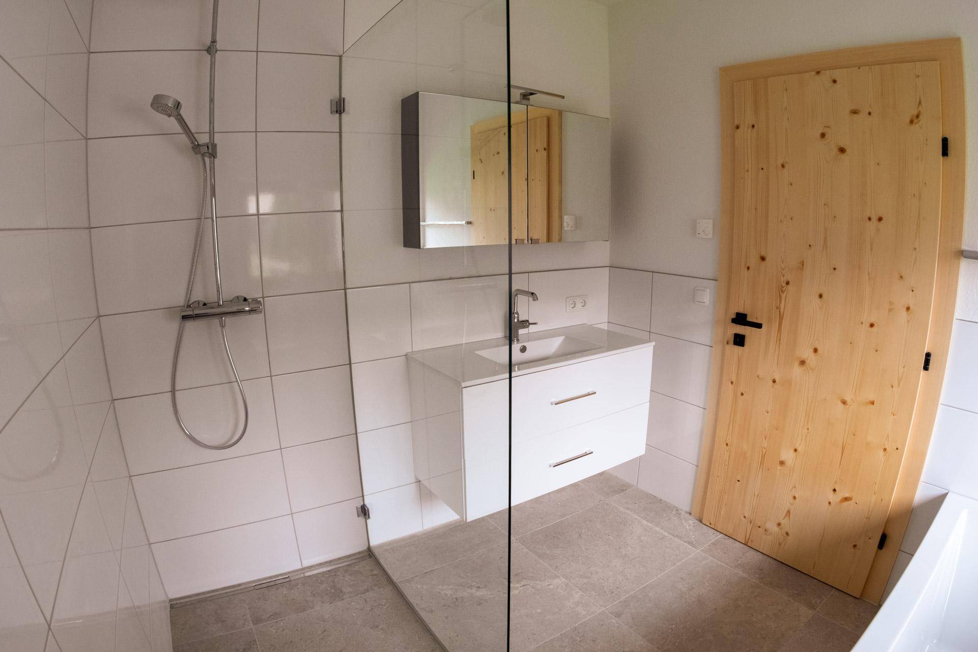 Modernes Badezimmer mit begehbarer Dusche, weißem Waschtisch und hellen Fliesen.