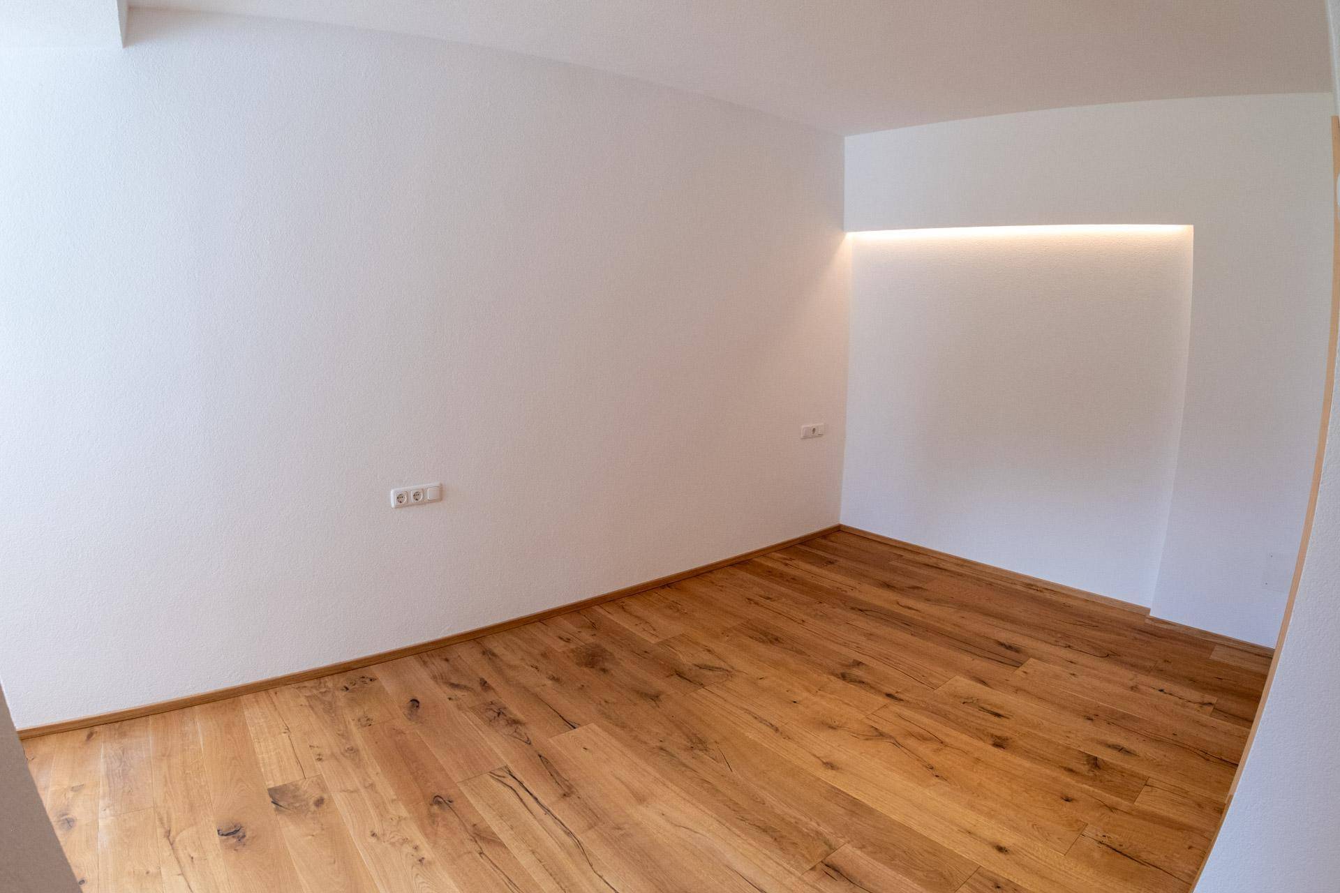 Ecke eines hellen Raumes mit Holzboden und einer modern beleuchteten Wandnische.