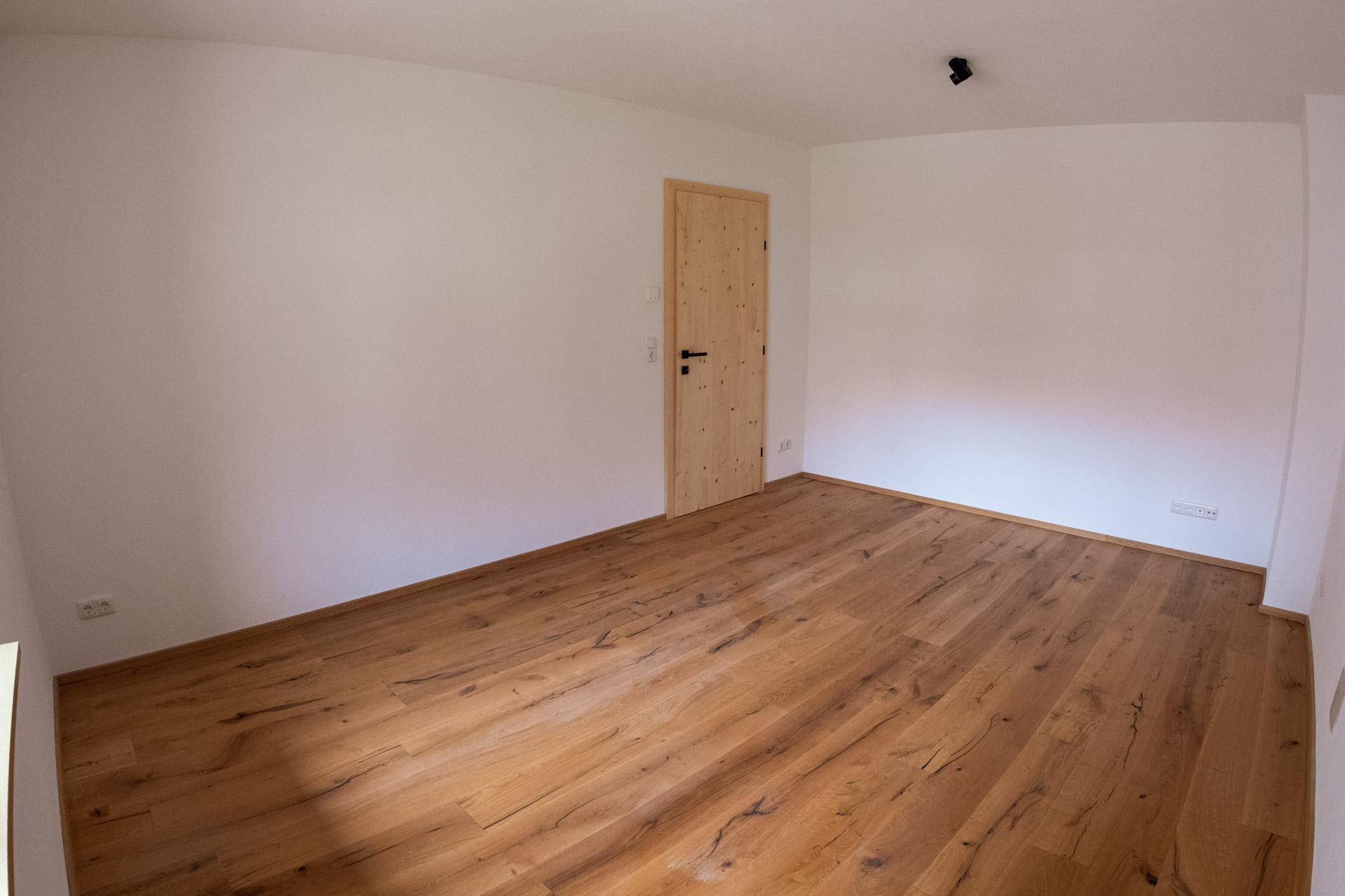 Geräumiges Schlafzimmer mit Holzboden, weißen Wänden und einer Holztür.