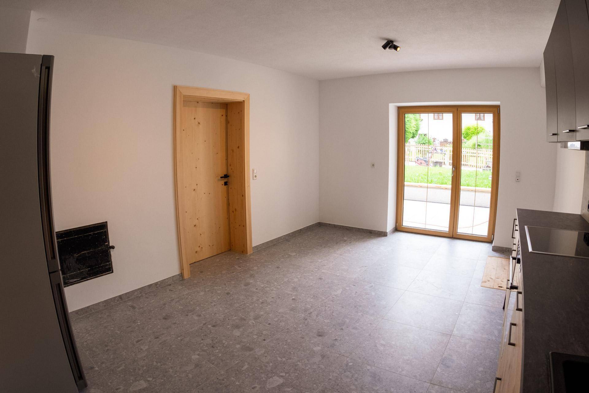 Geräumige Küche mit Fliesenboden, Kühlschrank und Zugang zu einem Außenbereich.