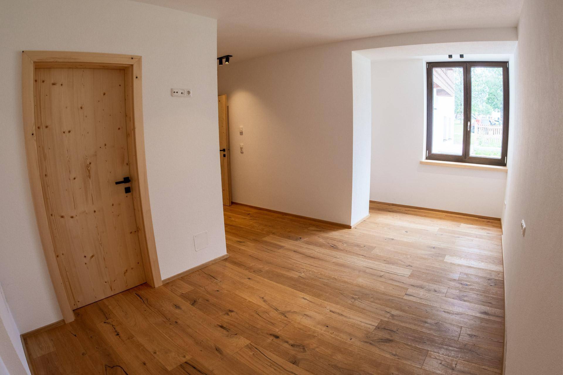 Heller Raum mit Holzboden, weißen Wänden und einem Fenster mit Blick nach draußen.