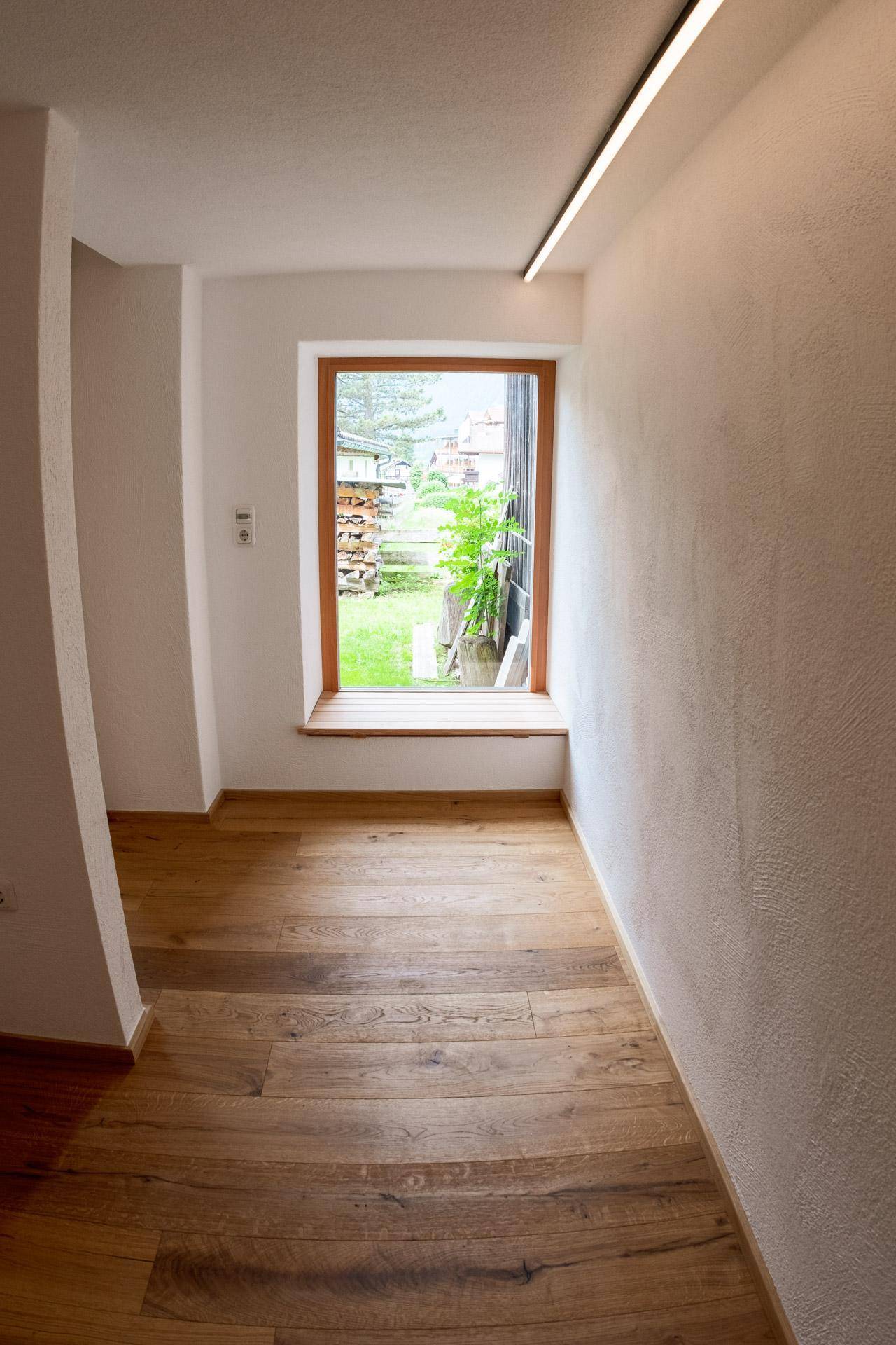 Heller Flur mit Holzboden und einem Fenster, das einen Blick ins Grüne bietet.