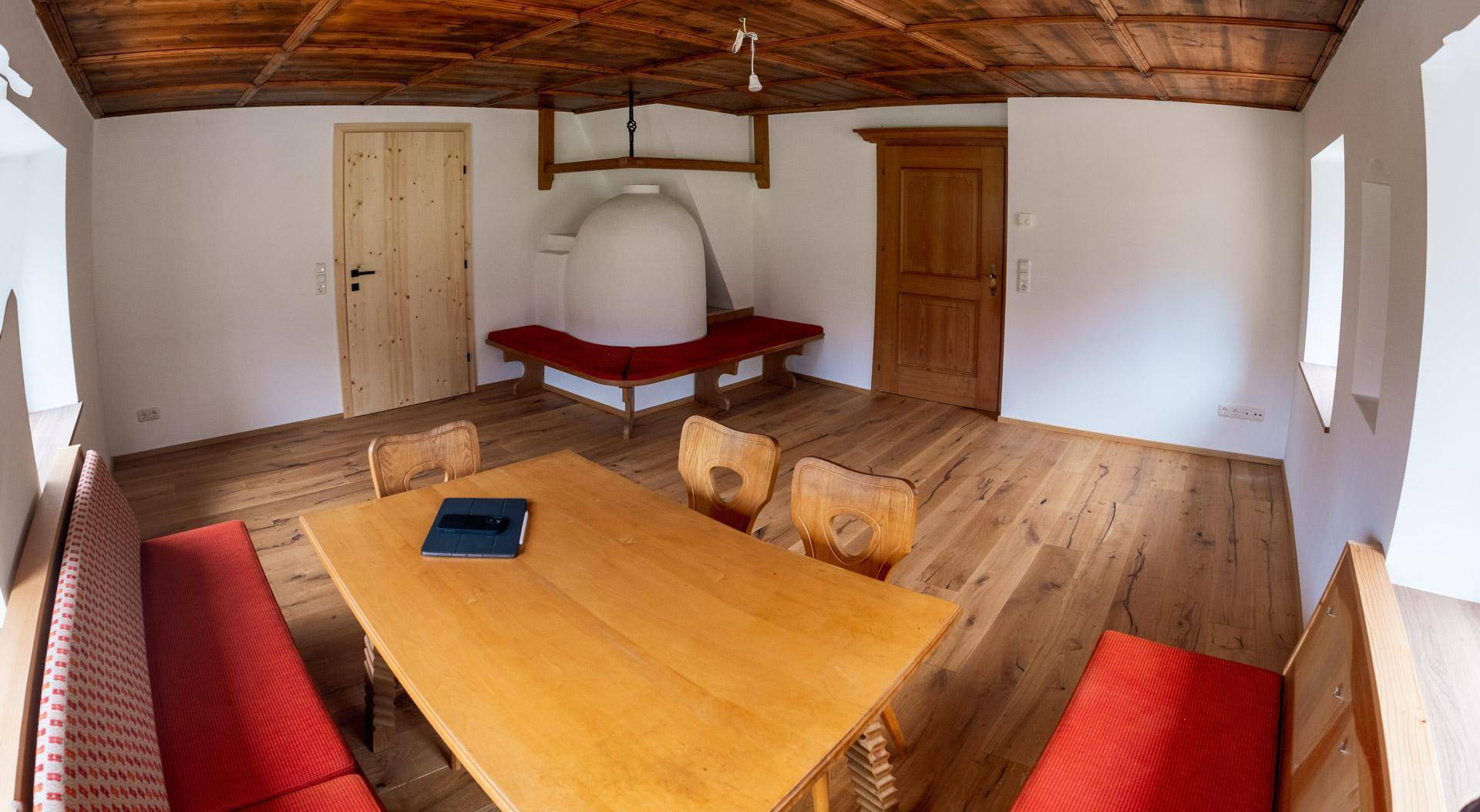 Detailansicht des Essbereichs mit Holztisch, Stühlen und dem traditionellen Kachelofen.