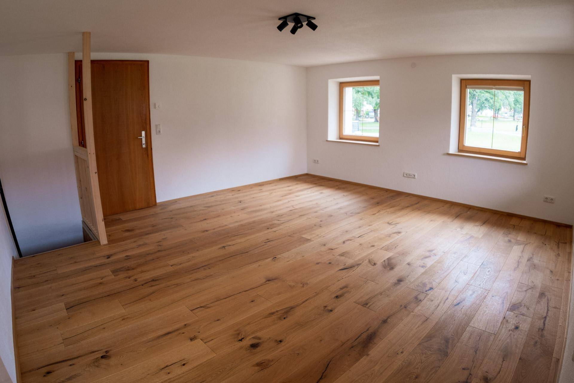 Heller Wohnraum mit Holzboden, weißen Wänden und zwei Fenstern.