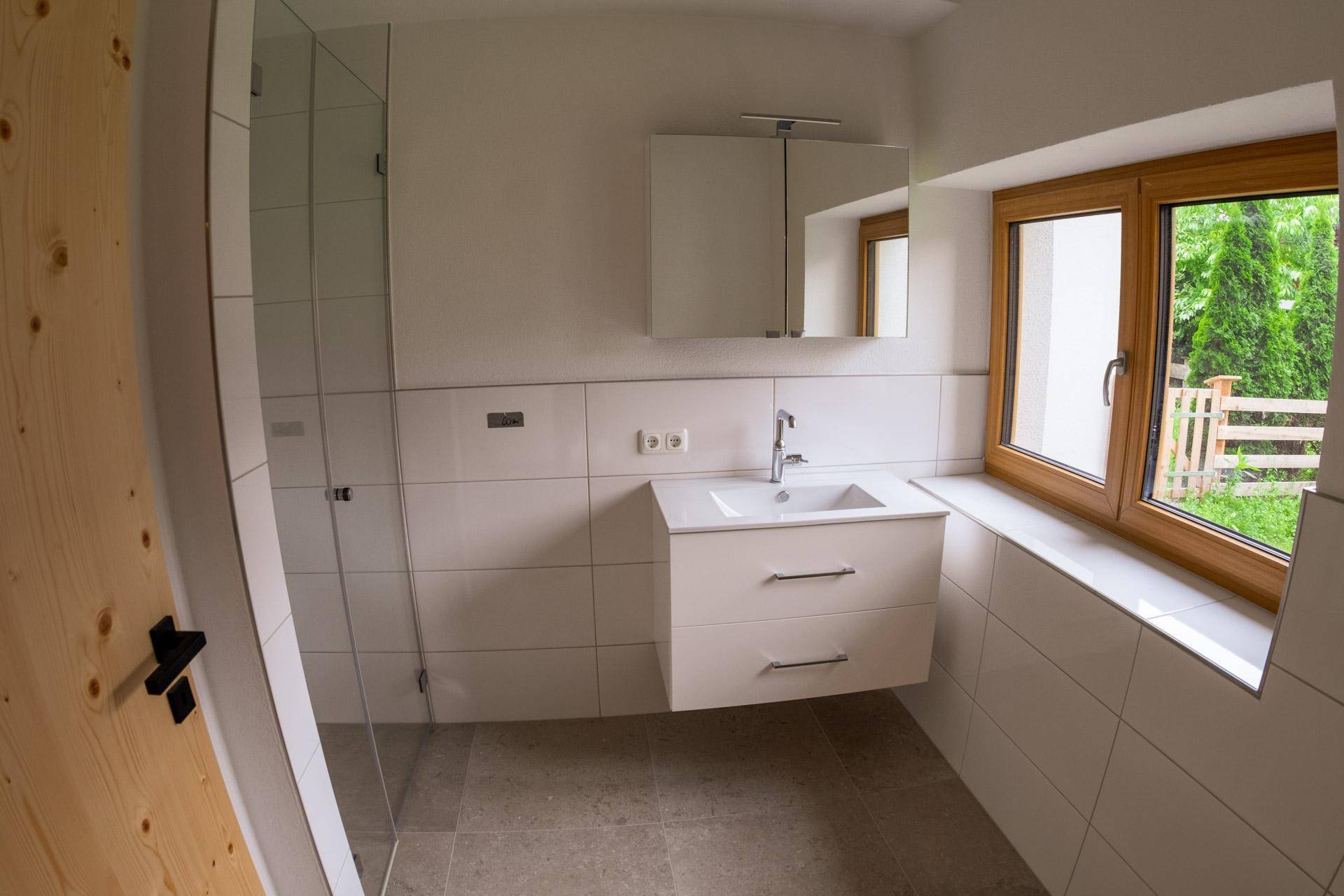 Modernes Badezimmer mit Dusche, Waschtisch, Spiegelschrank und Fenster mit Blick ins Grüne.