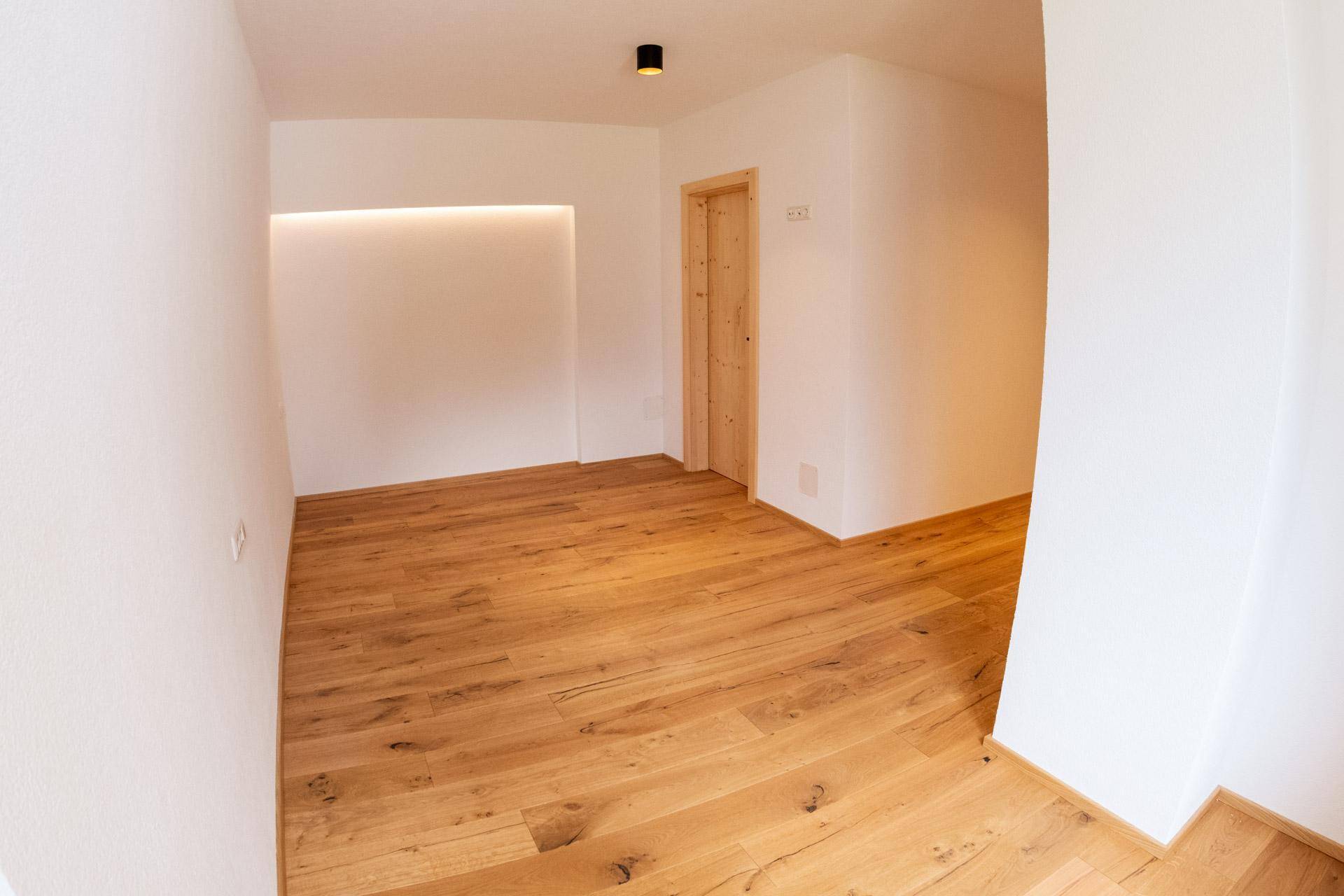 Geräumiger Raum mit Holzboden, weißen Wänden und einer beleuchteten Nische.