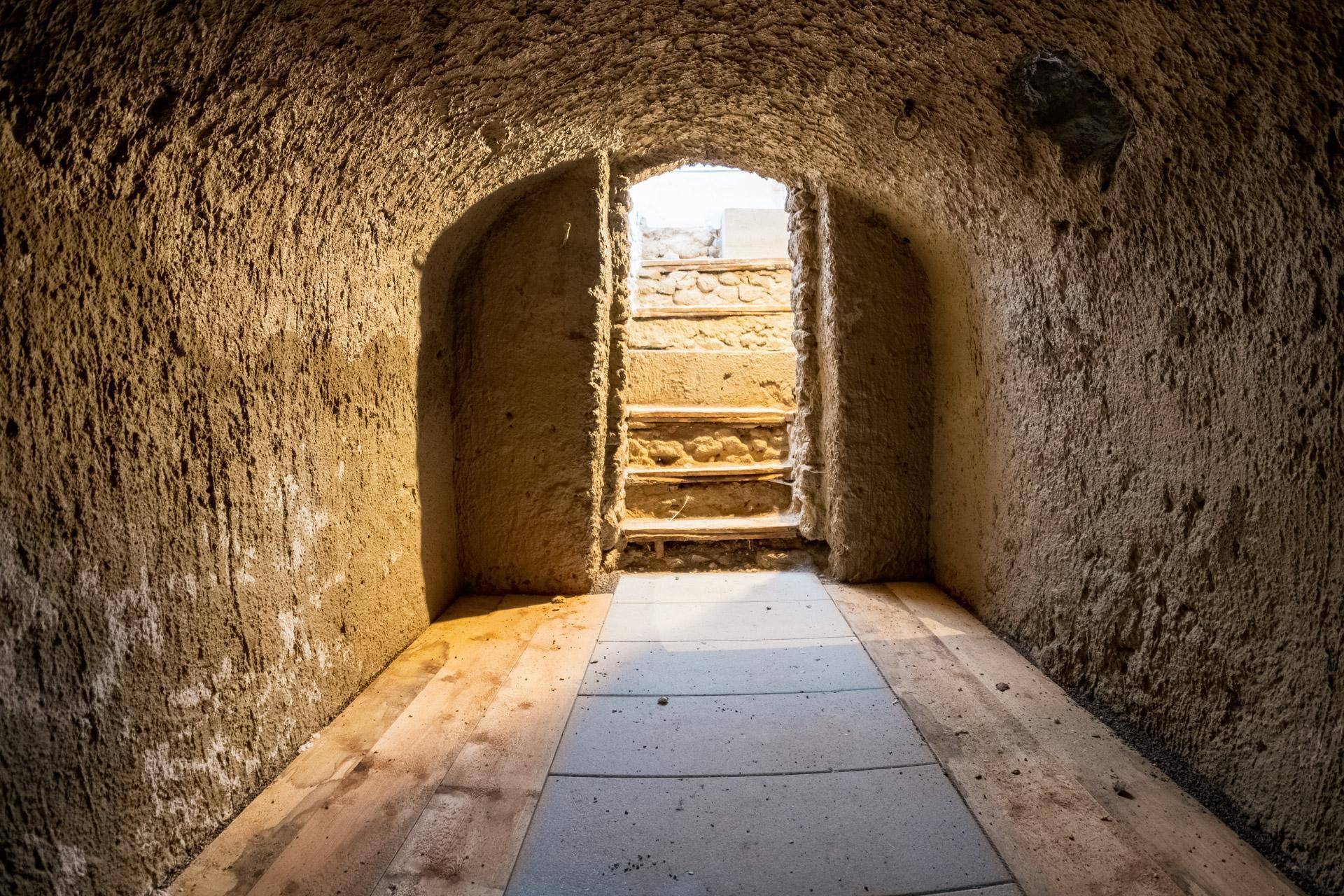 Rustikaler Kellergang mit Steinwänden und Holzdielen, der zu einer Treppe führt.