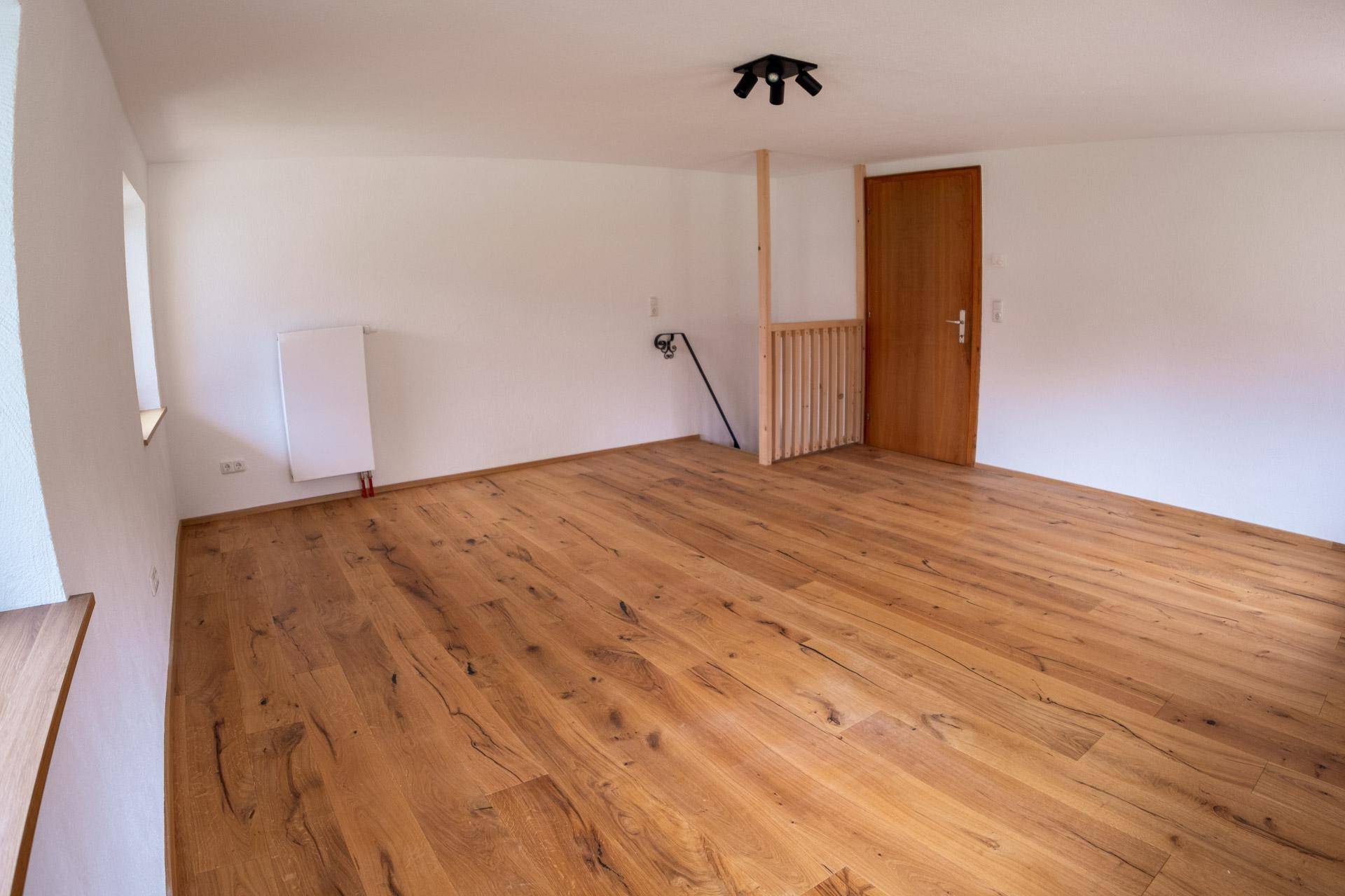 Geräumiger Wohnraum mit Holzboden, weißen Wänden und einem Heizkörper.