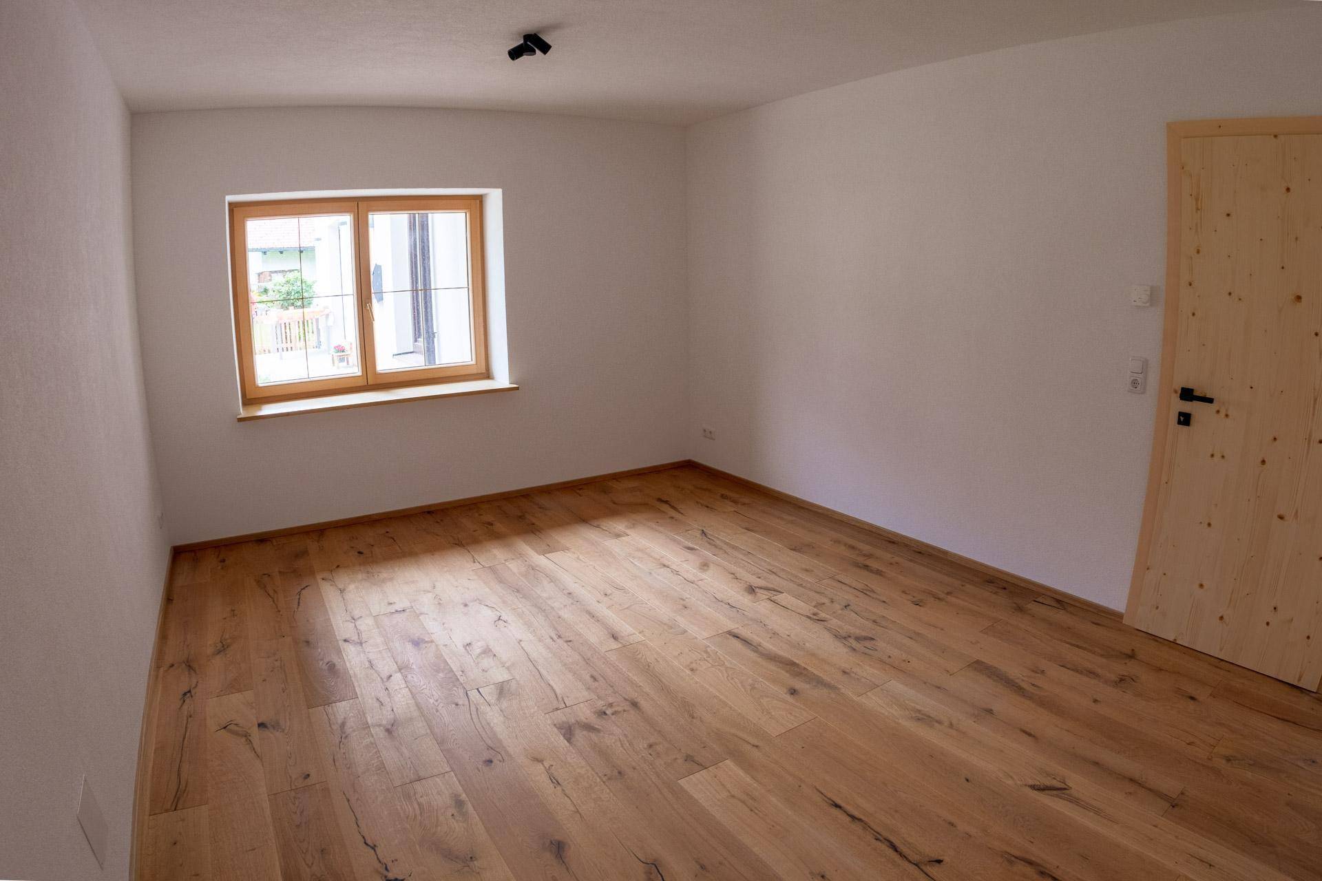 Helles Schlafzimmer mit Holzboden, weißen Wänden und einem Fenster mit Blick ins Grüne.