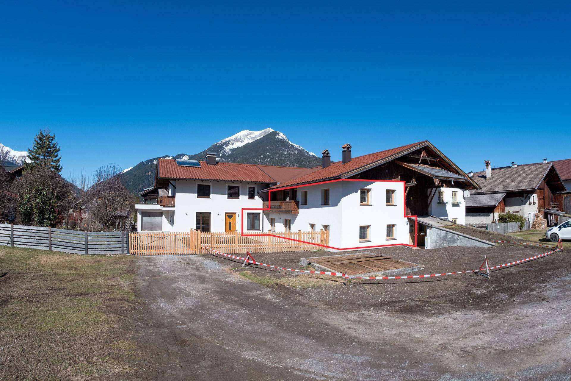 Außenansicht eines Hauses mit weißer Fassade, Holzzaun und Bergblick unter blauem Himmel.