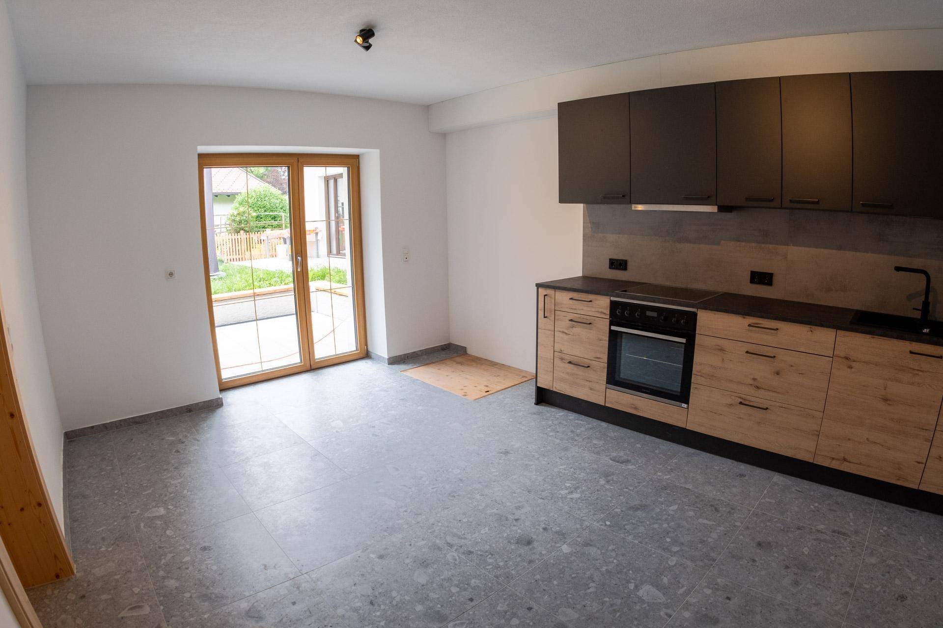 Helle Küche mit modernen Holz- und Grautönen, Fliesenboden und großer Terrassentür.