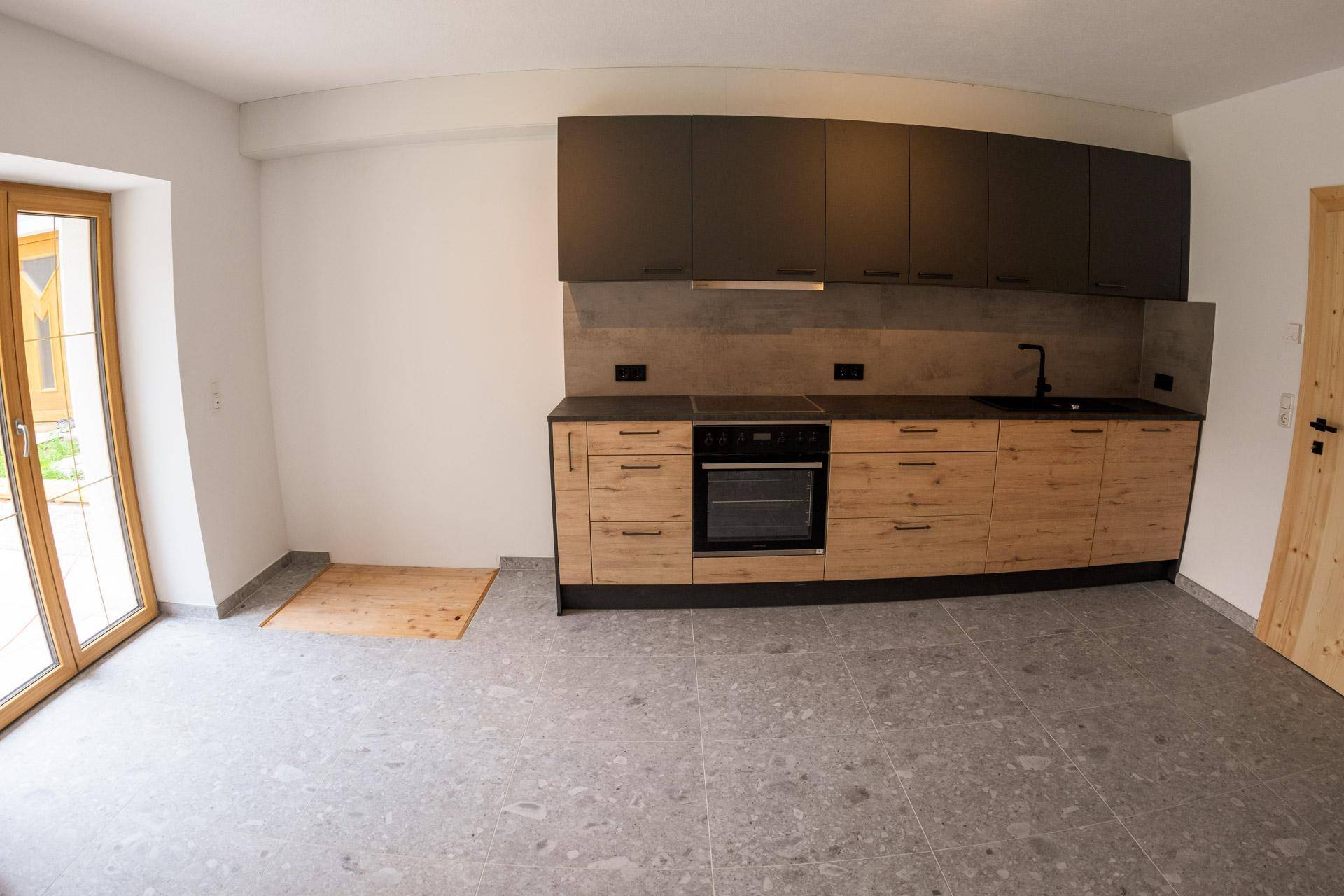 Moderne Einbauküche mit Holzfronten, dunklen Oberschränken und Zugang zum Außenbereich.