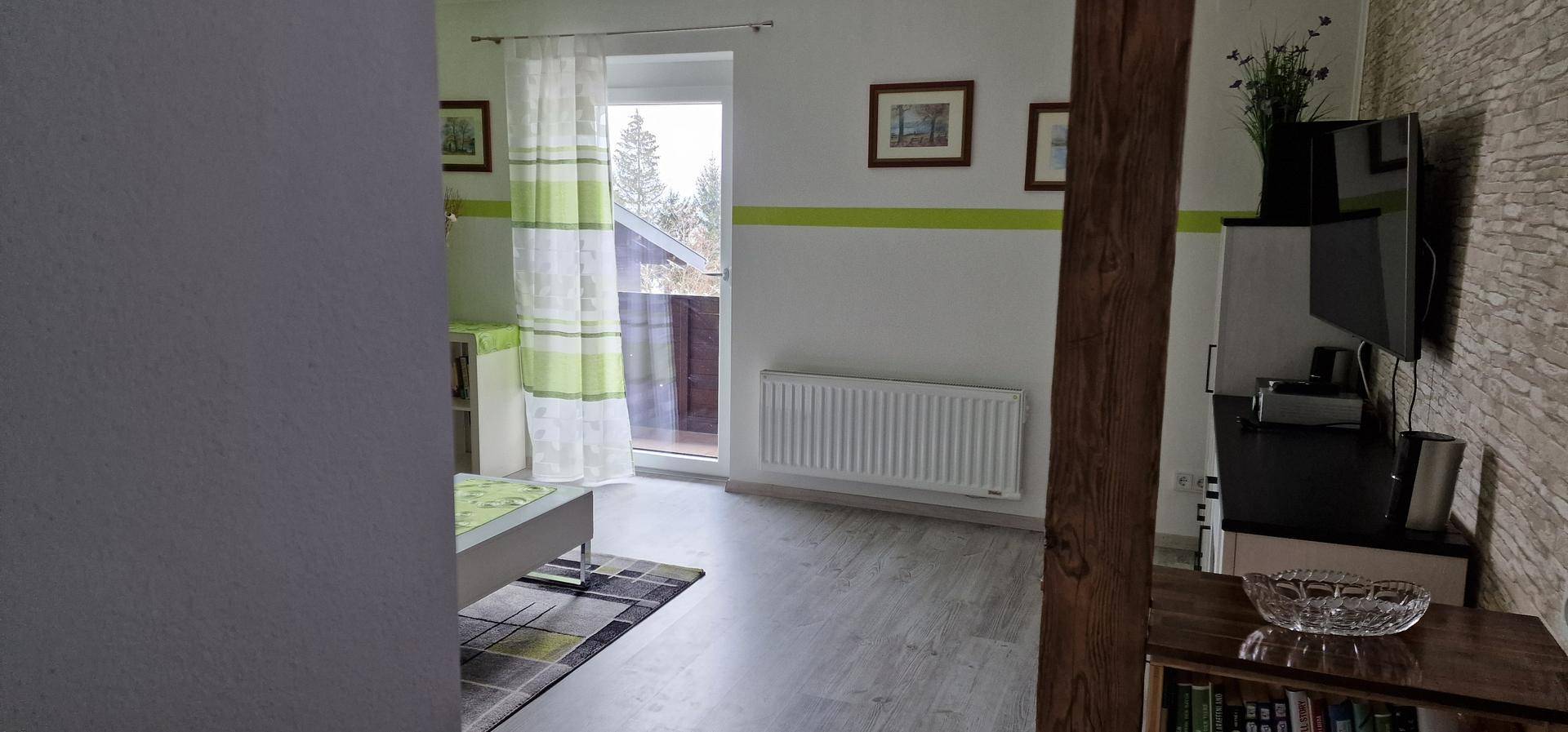 Heller Wohnbereich mit Zugang zum Balkon, Laminatboden und weißem Heizkörper unter dem Fenster.