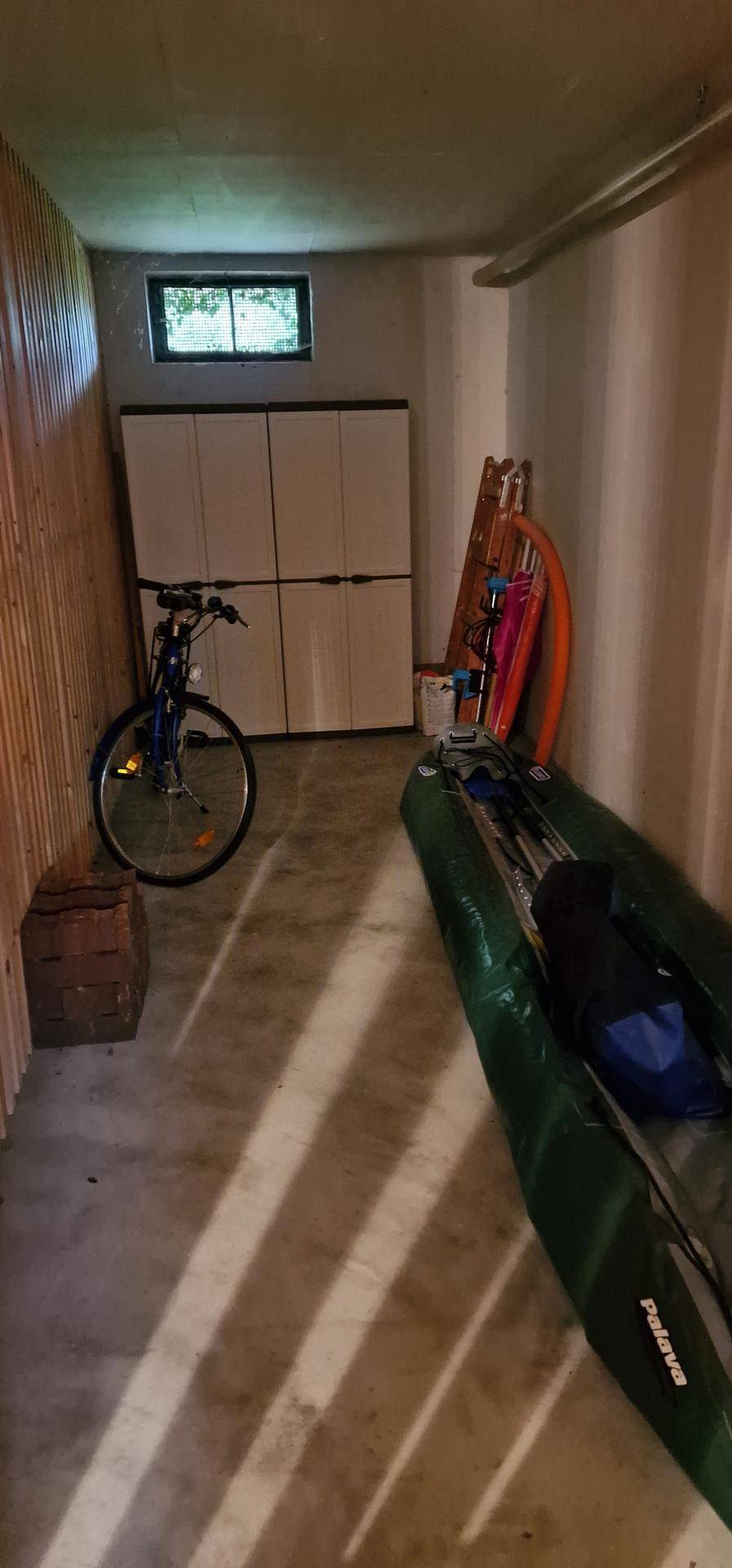 Kellerraum mit Fahrrad, aufblasbarem Boot und Lagerschränken, gut beleuchtet durch ein kleines Fenster.