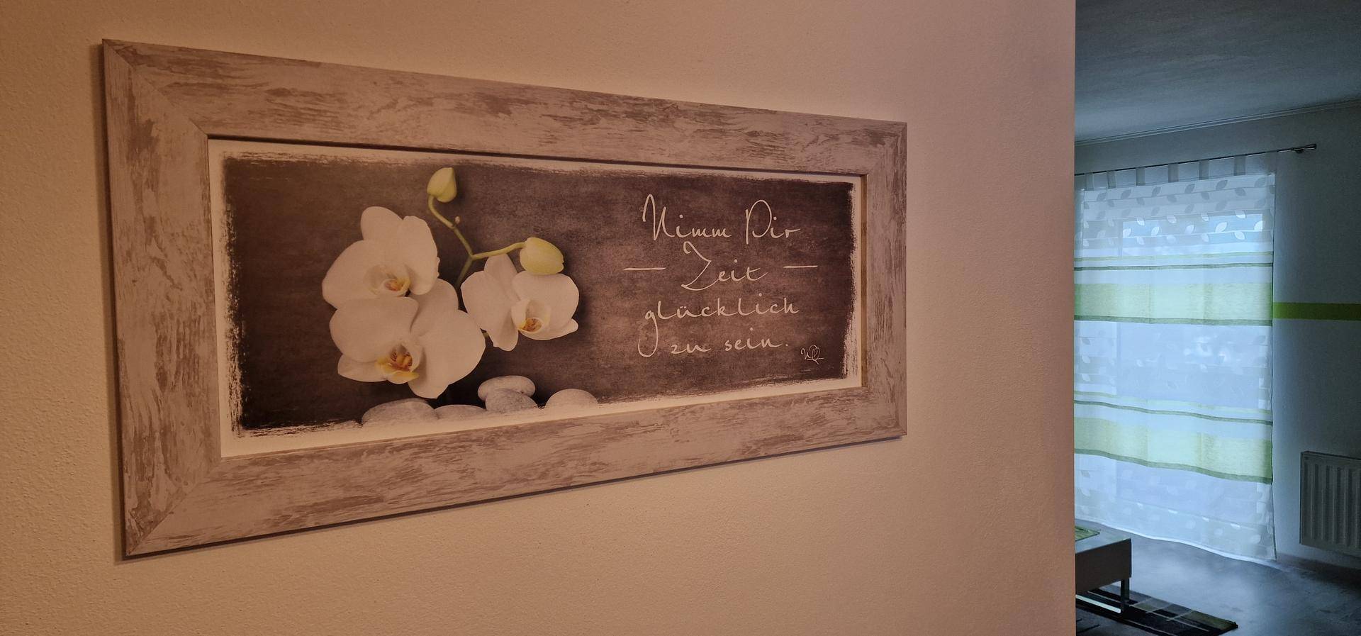 Wanddekoration mit Orchideenmotiv und inspirierendem Spruch, neben einem hellen Fensterbereich.