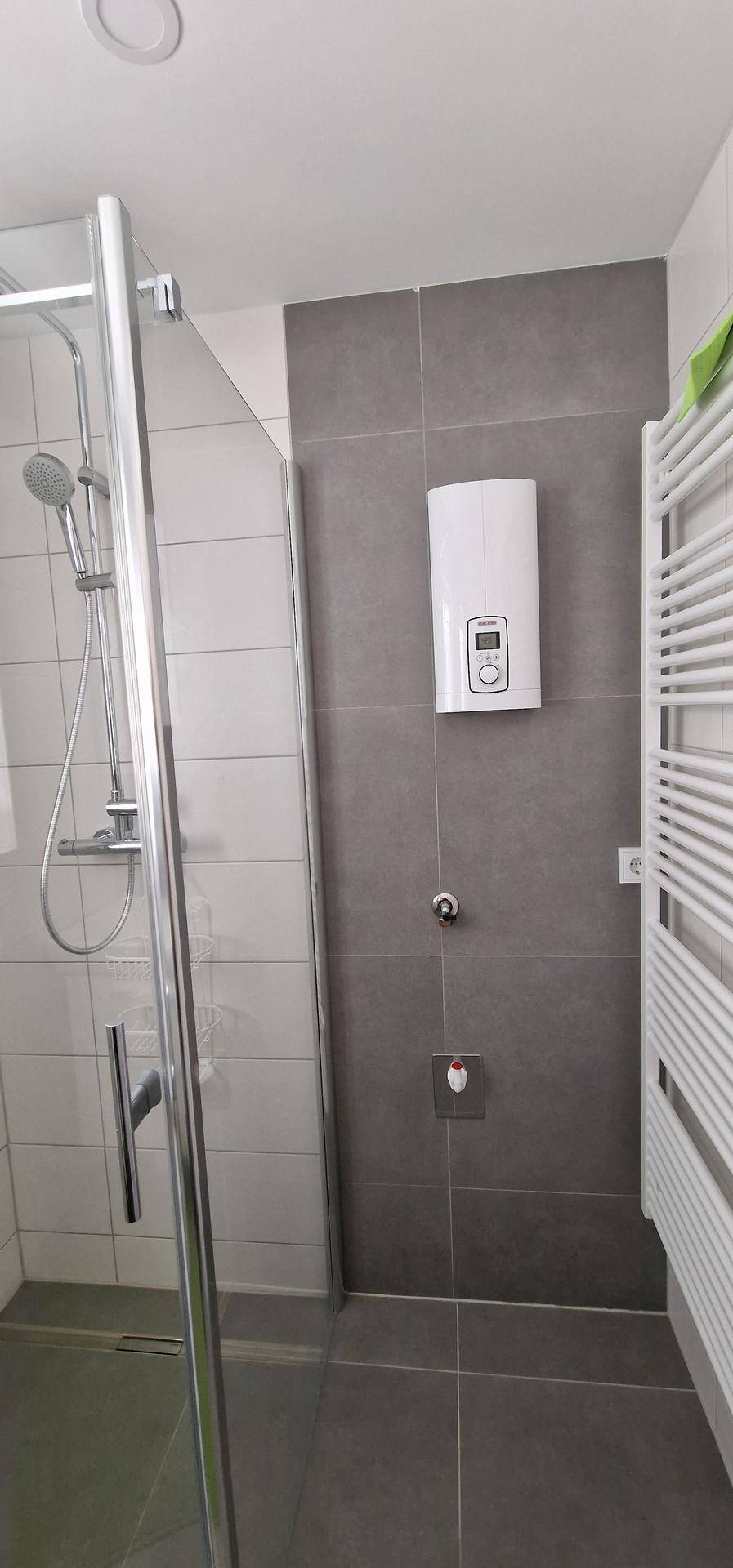 Duschkabine mit Glaswand, grauen Fliesen und einem Handtuchheizkörper an der Wand.