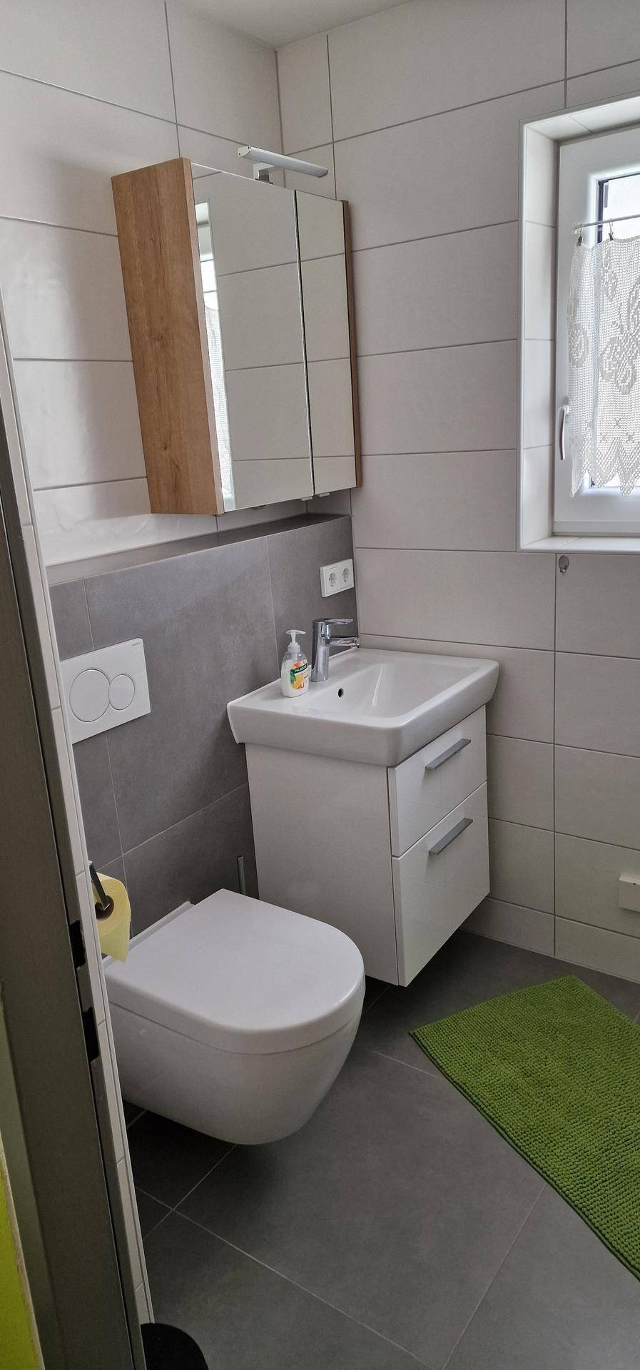 Modernes Badezimmer mit Wand-WC, Waschbecken und Spiegelschrank, in hellen Grautönen gehalten.